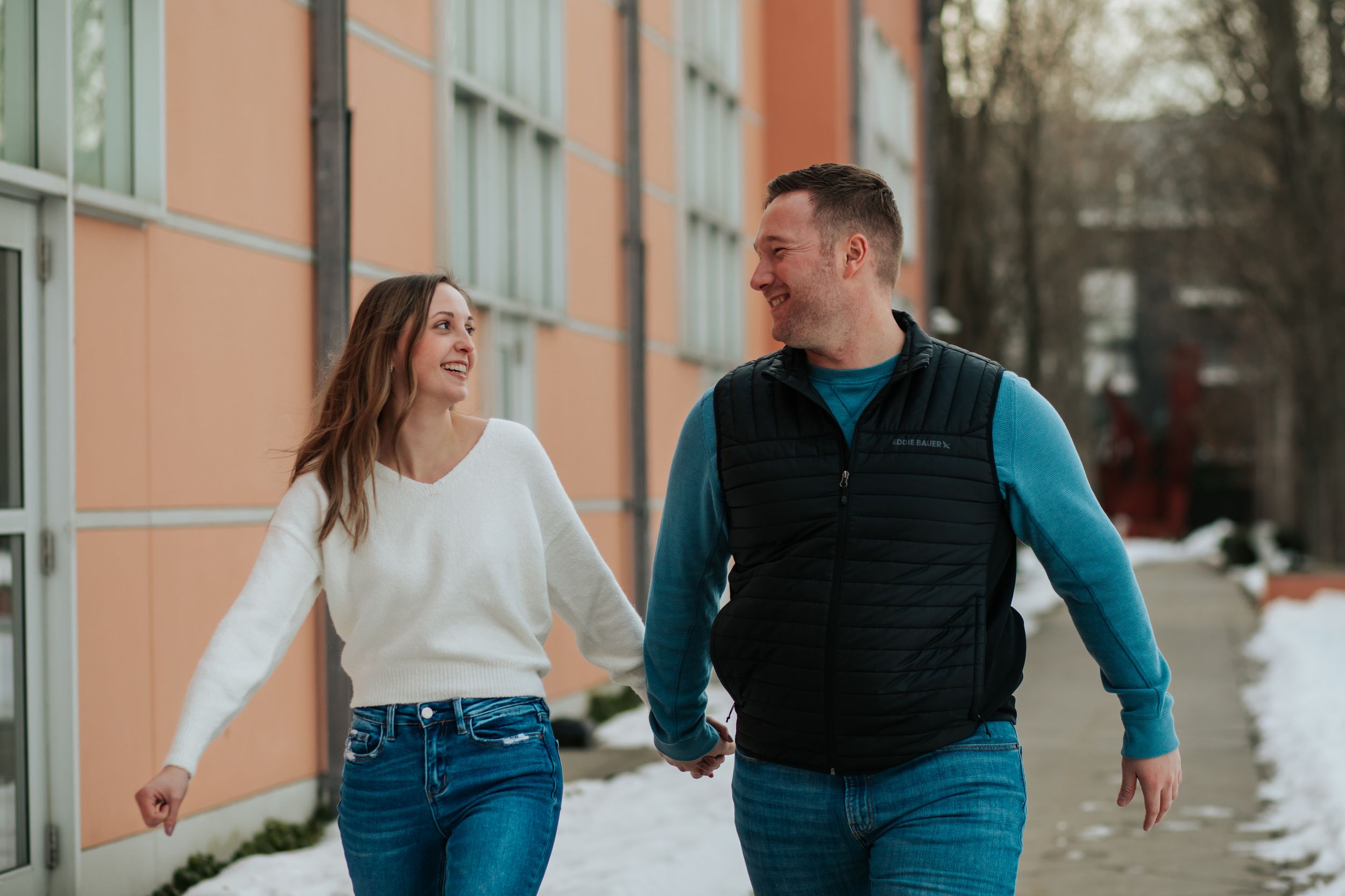 Couple shares playful moment against peach-colored wall in winter setting.