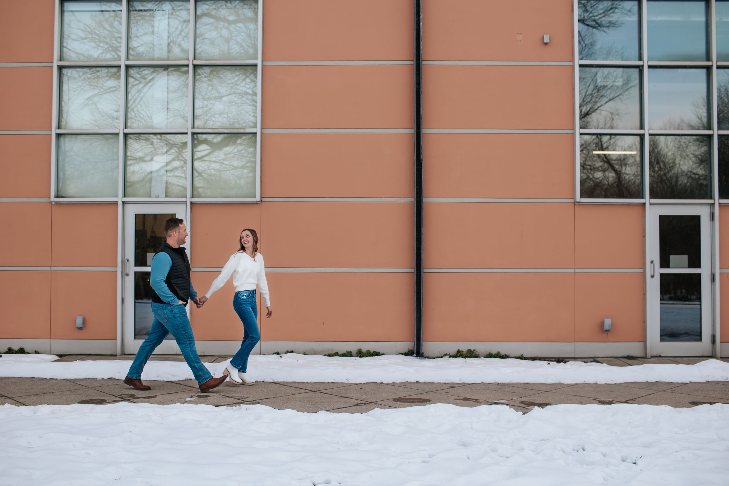 A panoramic view of a person walking past an orange and white building facade in snowy winter conditions.