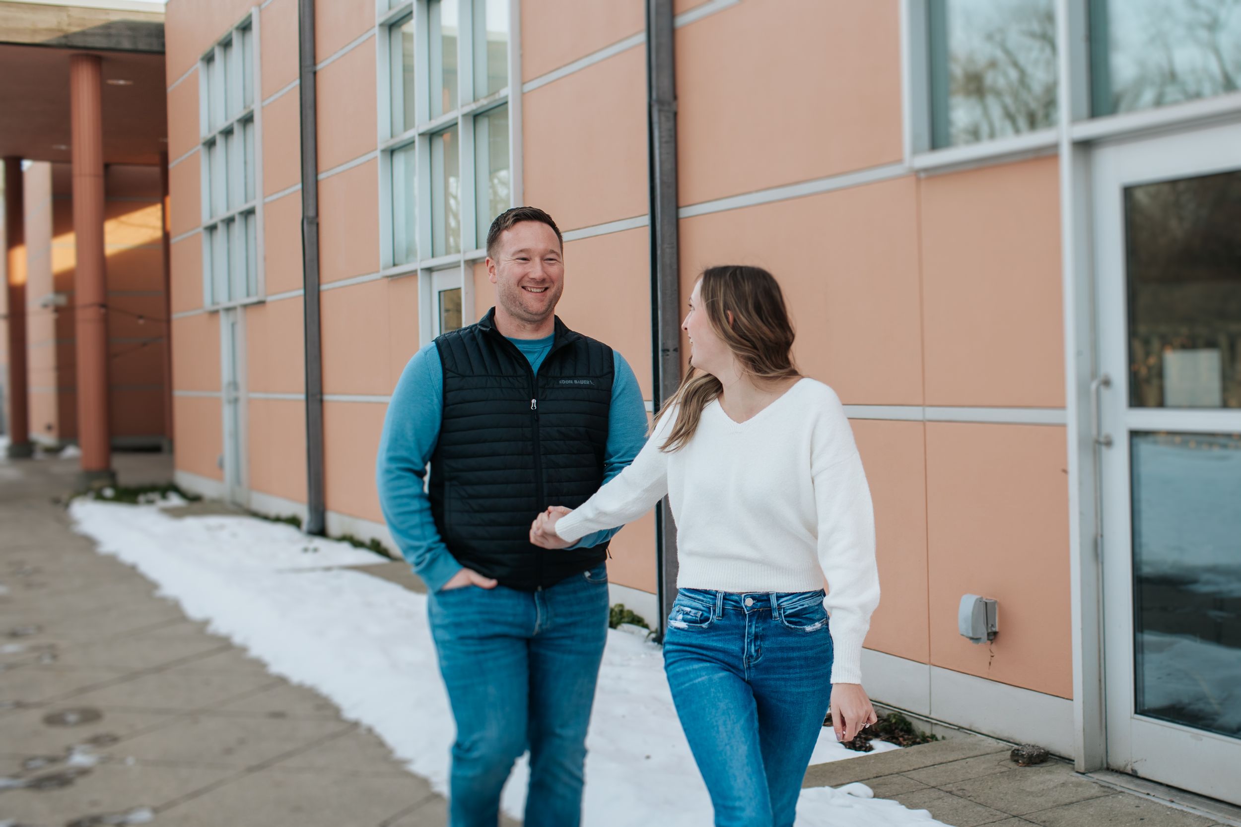 Couple interacts playfully outside a modern building with peach-colored walls.