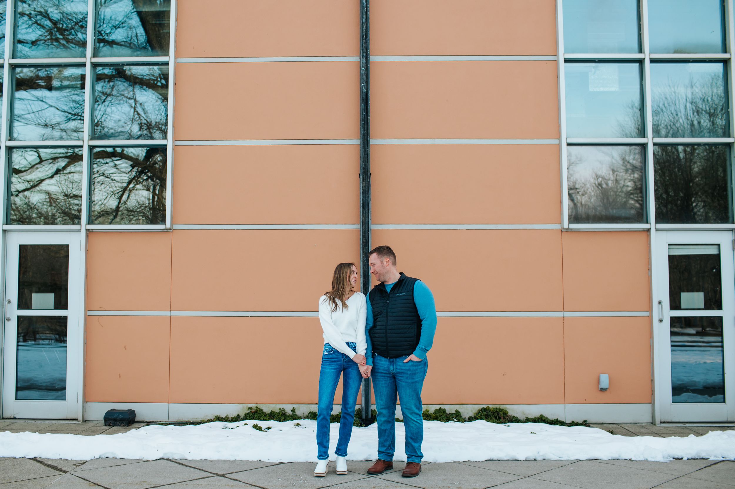 Couple stands together against modern building exterior with windows.