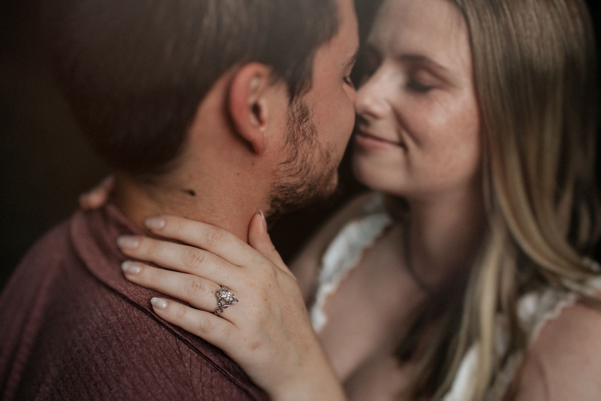 Romantic couple sharing tender moments in golden sunlit field during sunset engagement photoshoot.