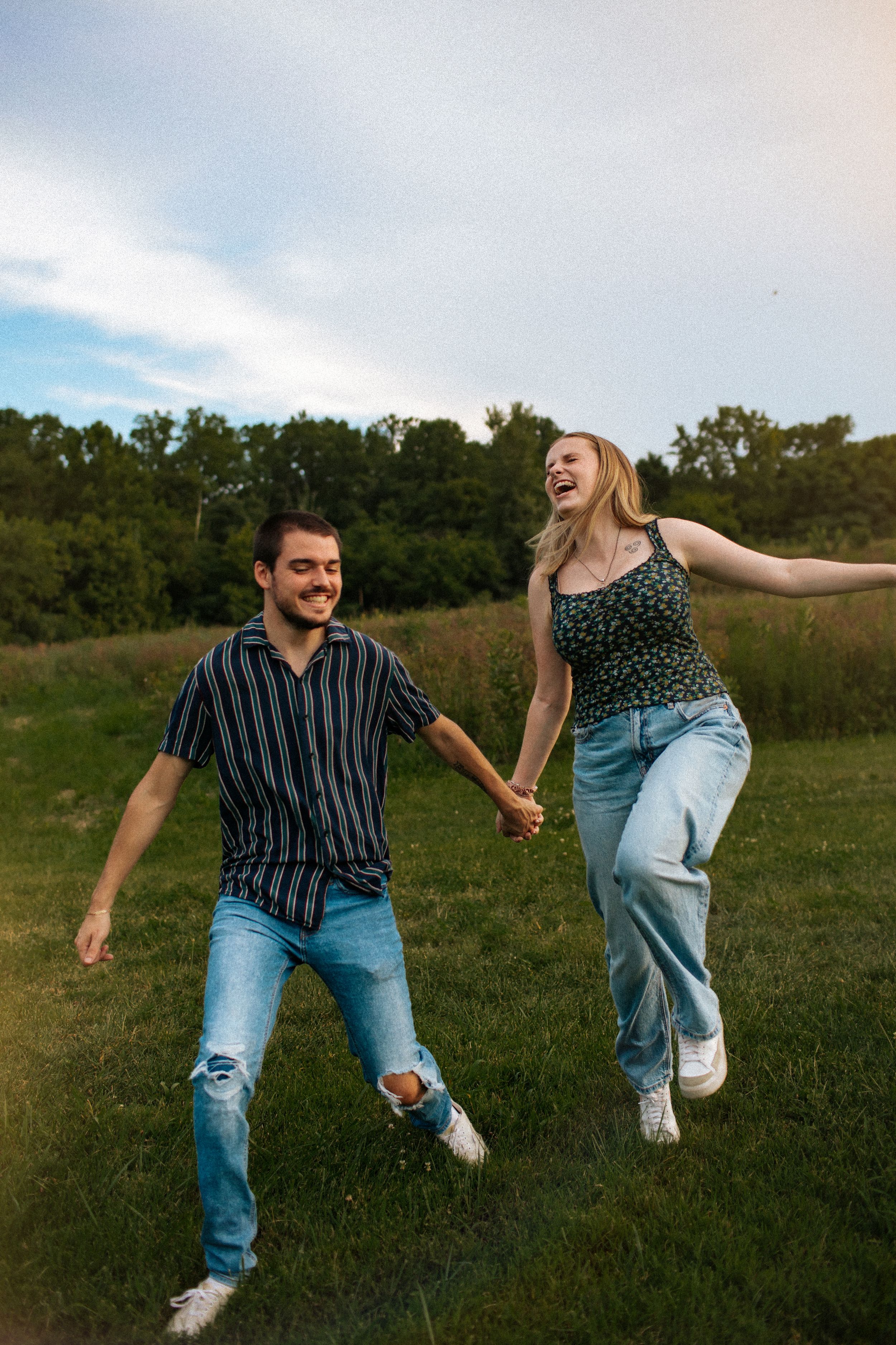 A playful couple jumps and holds hands while enjoying a sunny day in a grassy field.