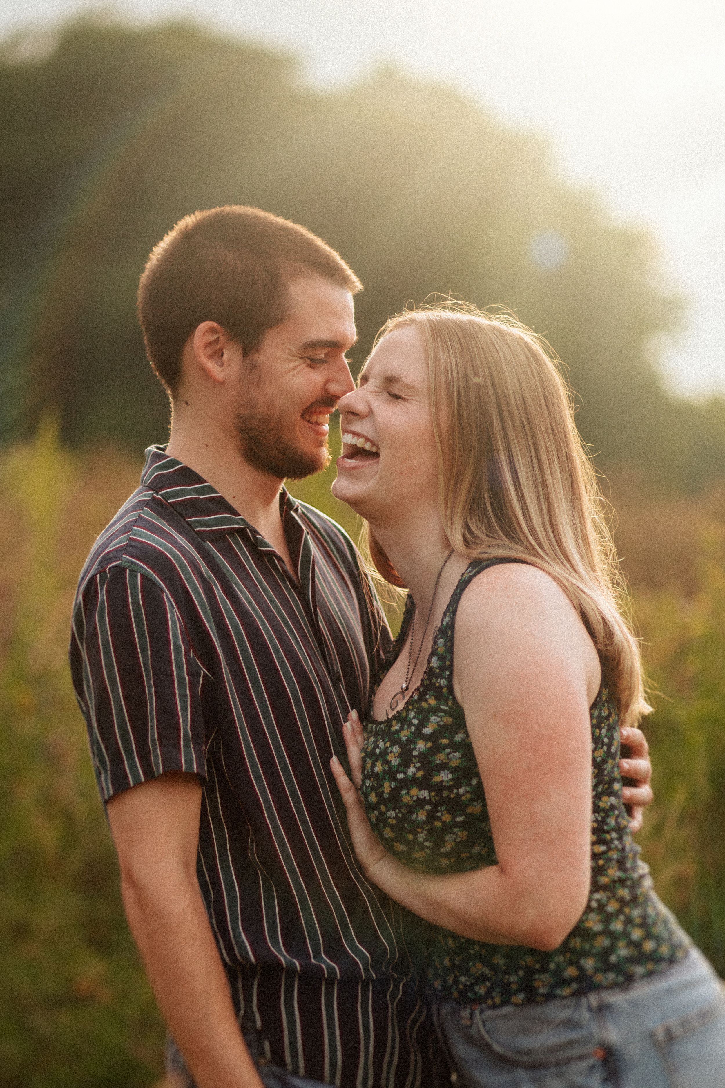 A couple shares an intimate laughing moment together at sunset in a natural outdoor setting.