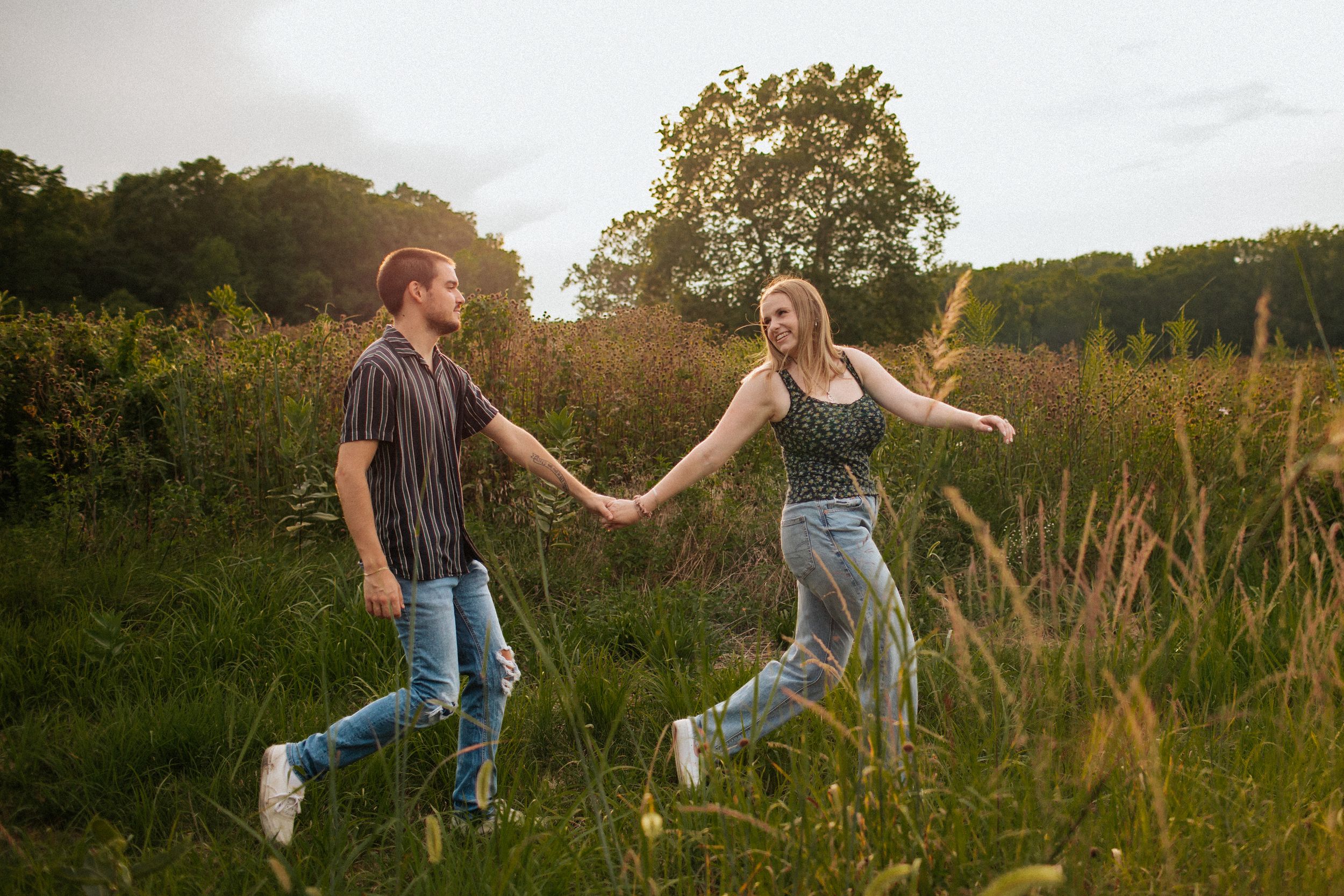 People dancing and twirling in a golden sunlit meadow at sunset with tall grass and trees in the background.