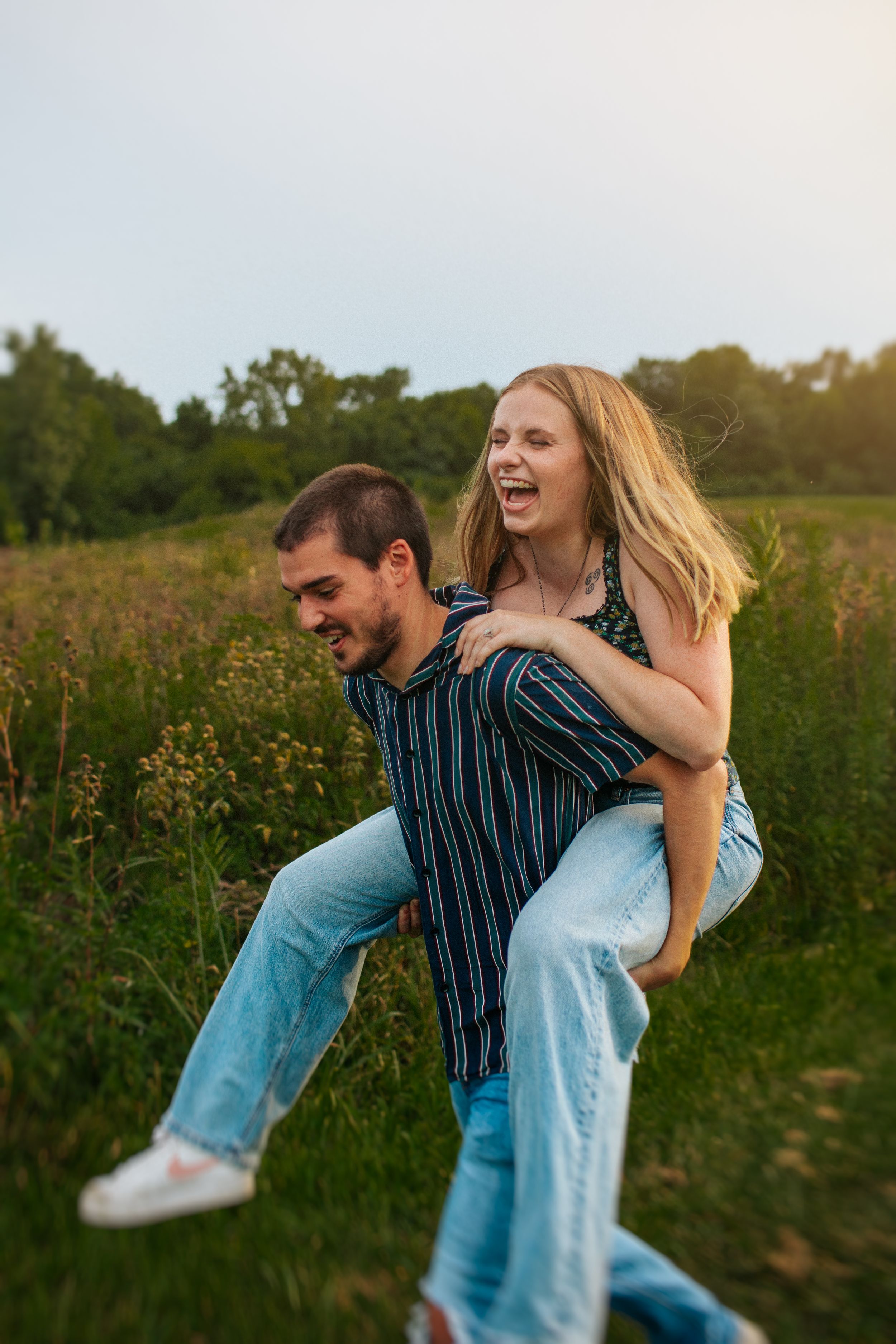 A couple shares a playful piggyback ride moment in a wildflower meadow during golden hour.