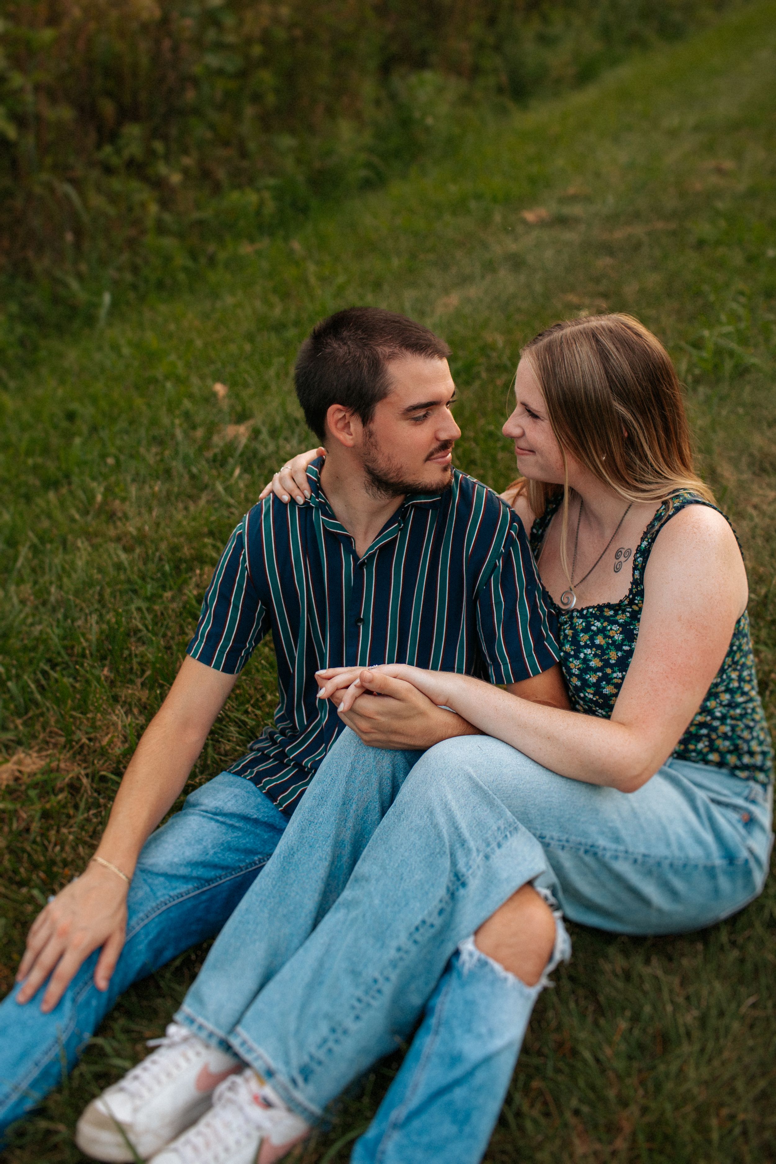 Couple sitting together on grass wearing casual denim and stripes in an intimate outdoor setting.