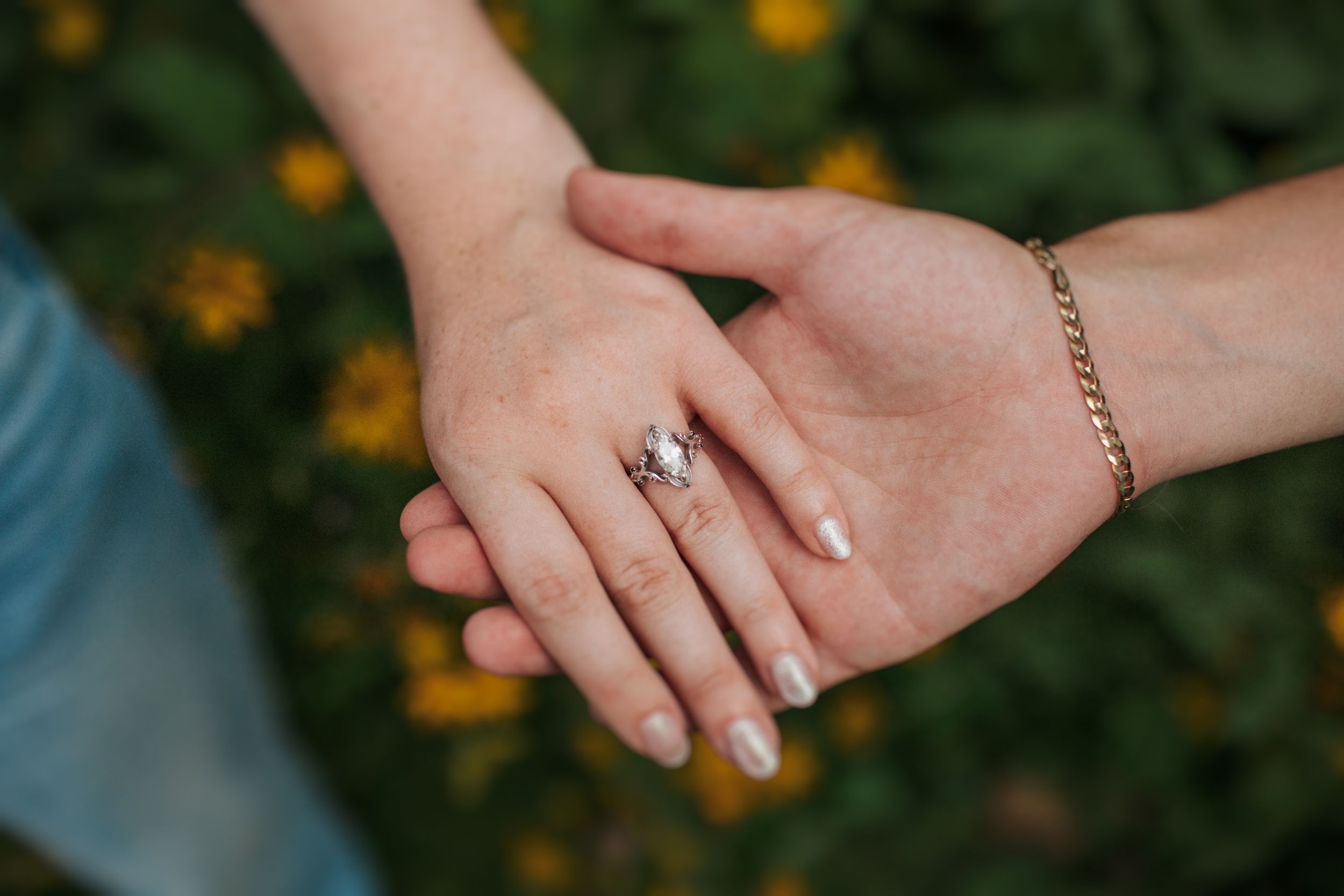 Close-up view of hands with engagement ring against a blurred natural background.