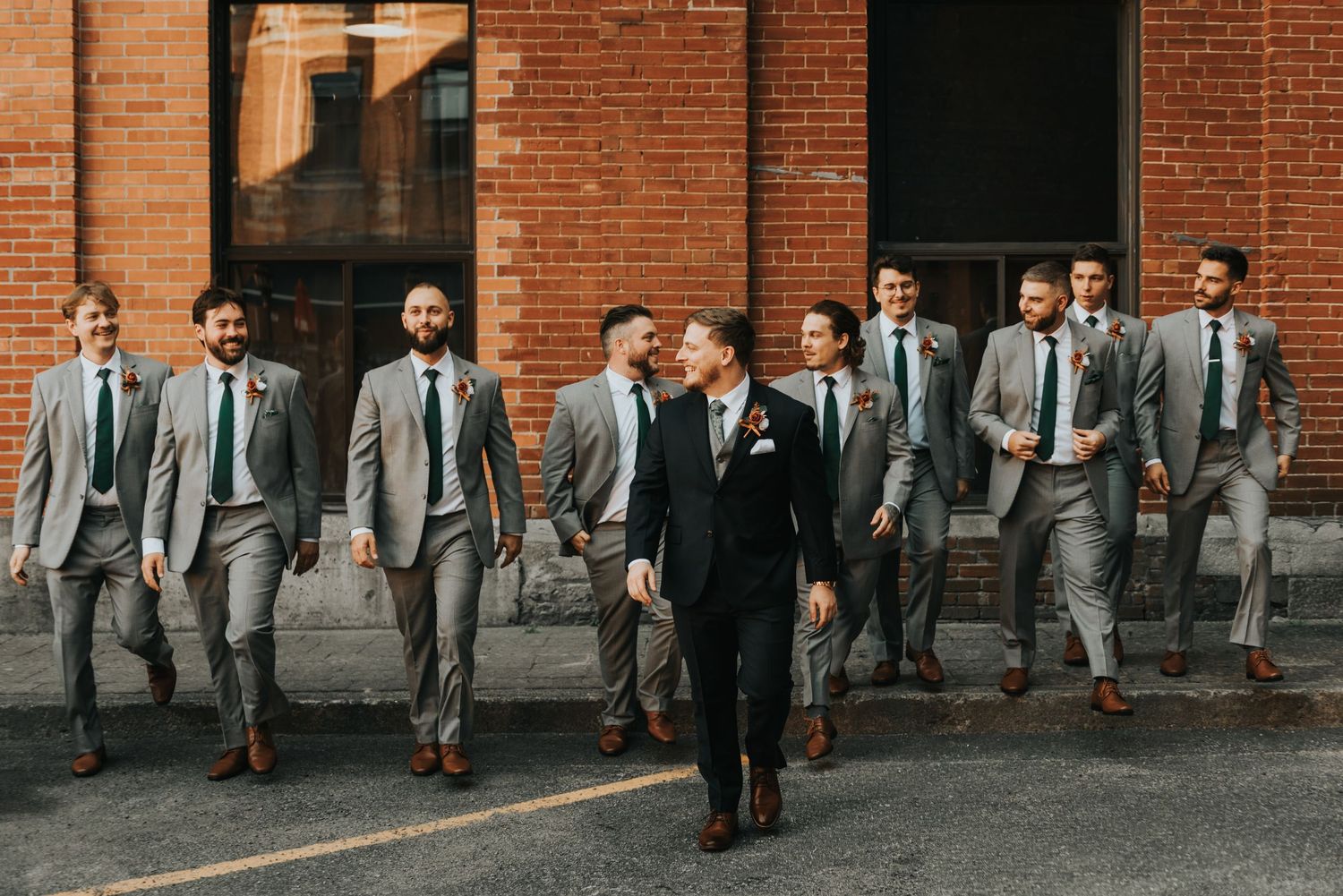 Wedding party in gray suits walking along a brick wall in an urban setting.