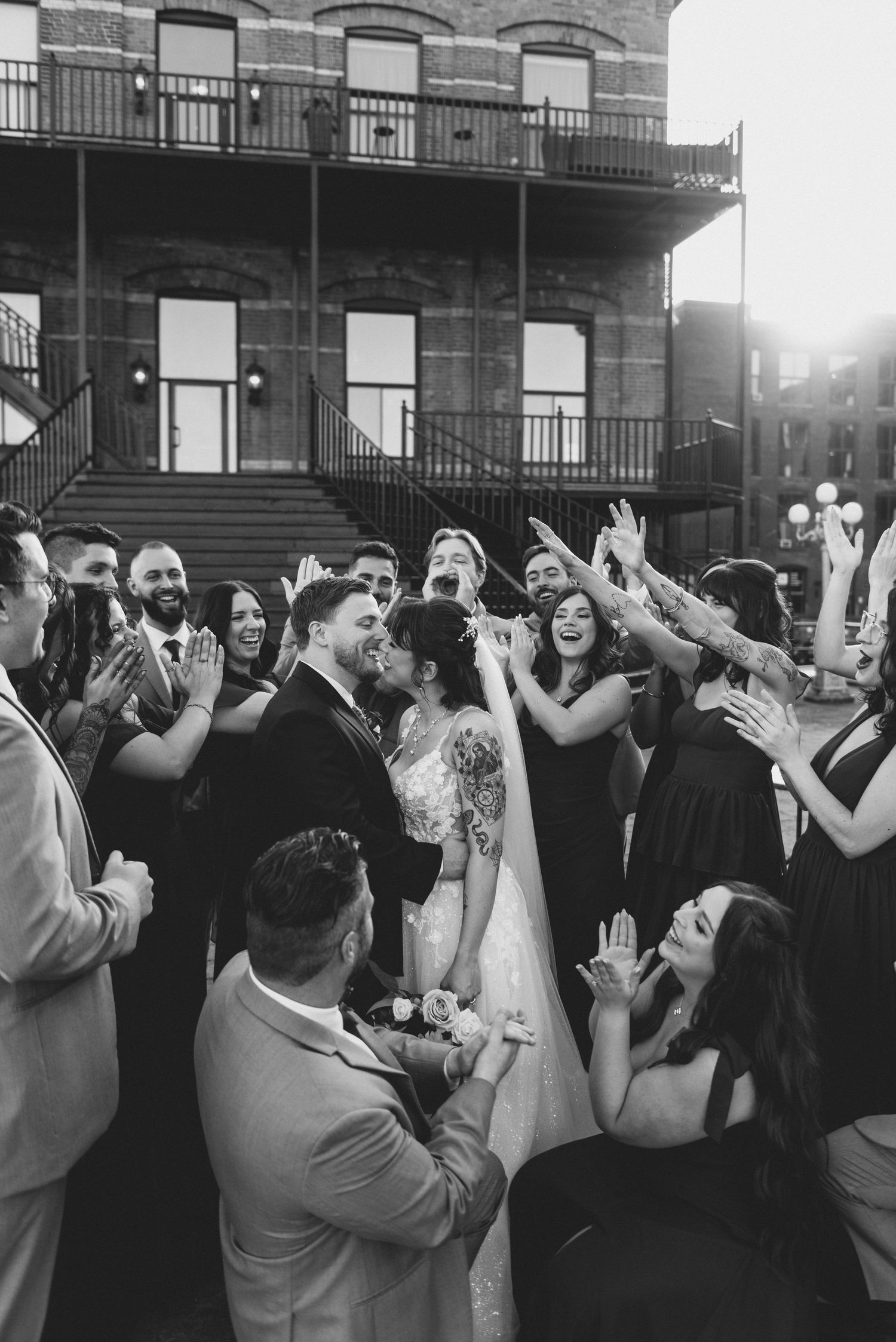 A joyous wedding celebration with guests dancing and celebrating on an outdoor patio with historic architecture in background.