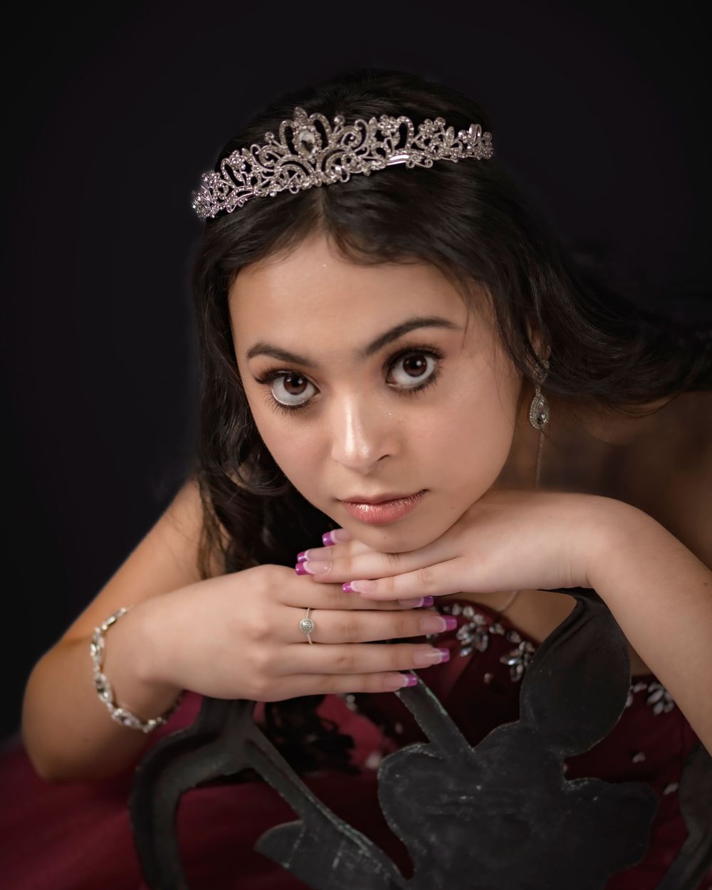 Close-up portrait of a teenage girl wearing a tiara and burgundy dress for her quinceañera.
