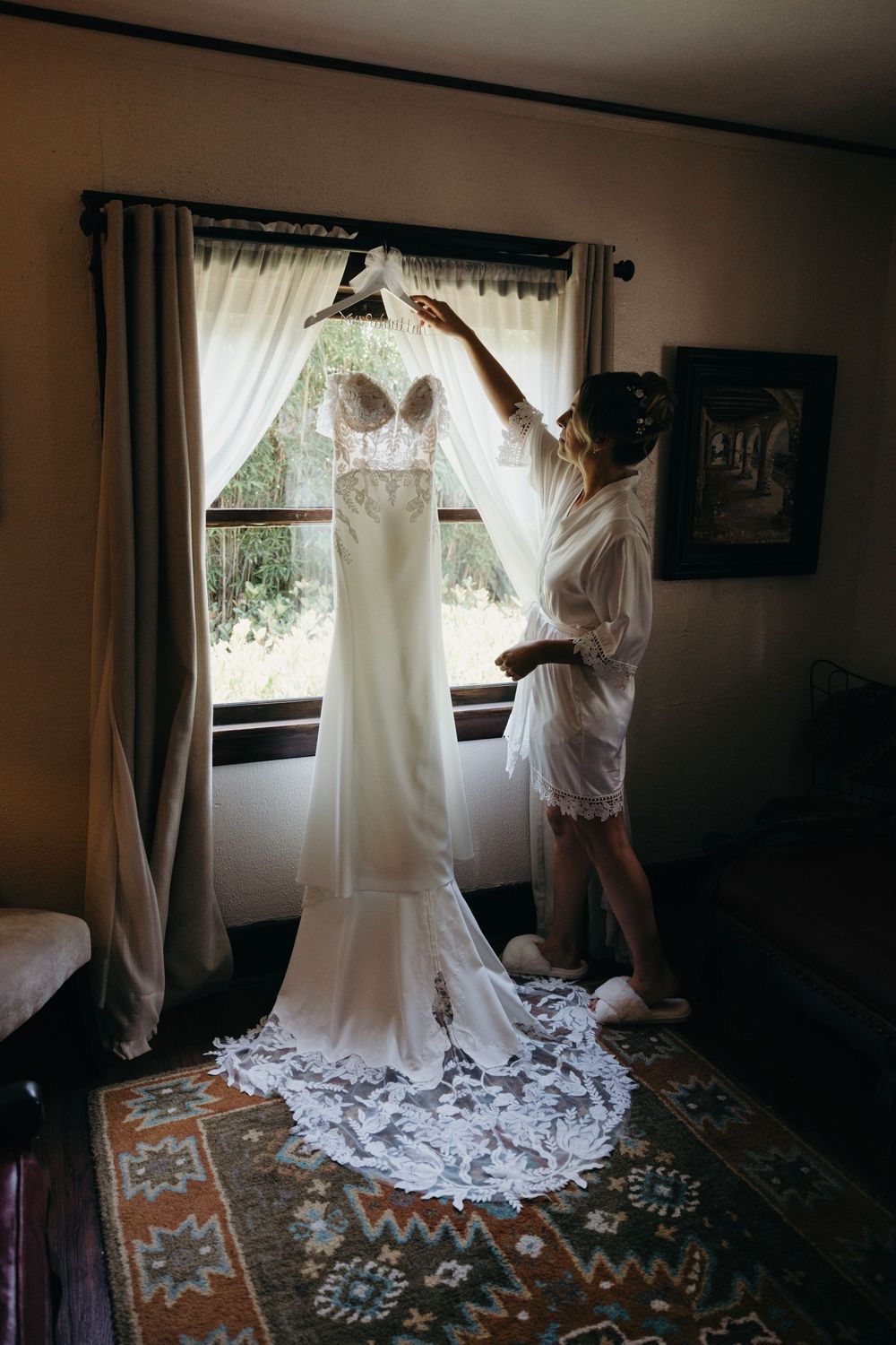 White wedding gown being prepared in a sunlit room with decorative carpet.