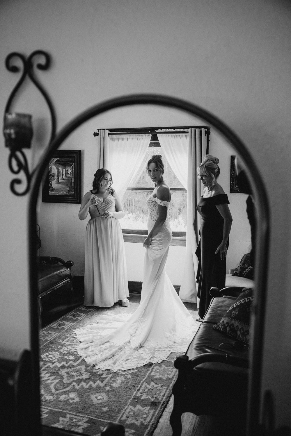 Black and white mirror reflection captures wedding dress preparations in intimate setting.