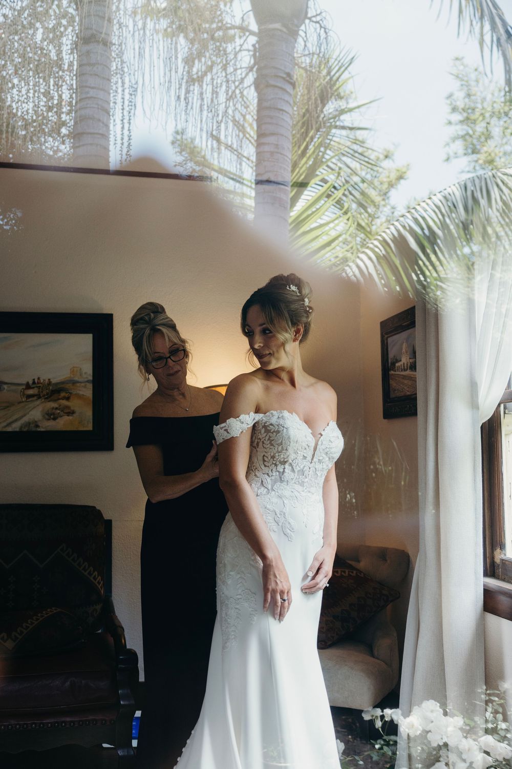 Final wedding dress fitting in sunlit room with palm trees visible through windows.