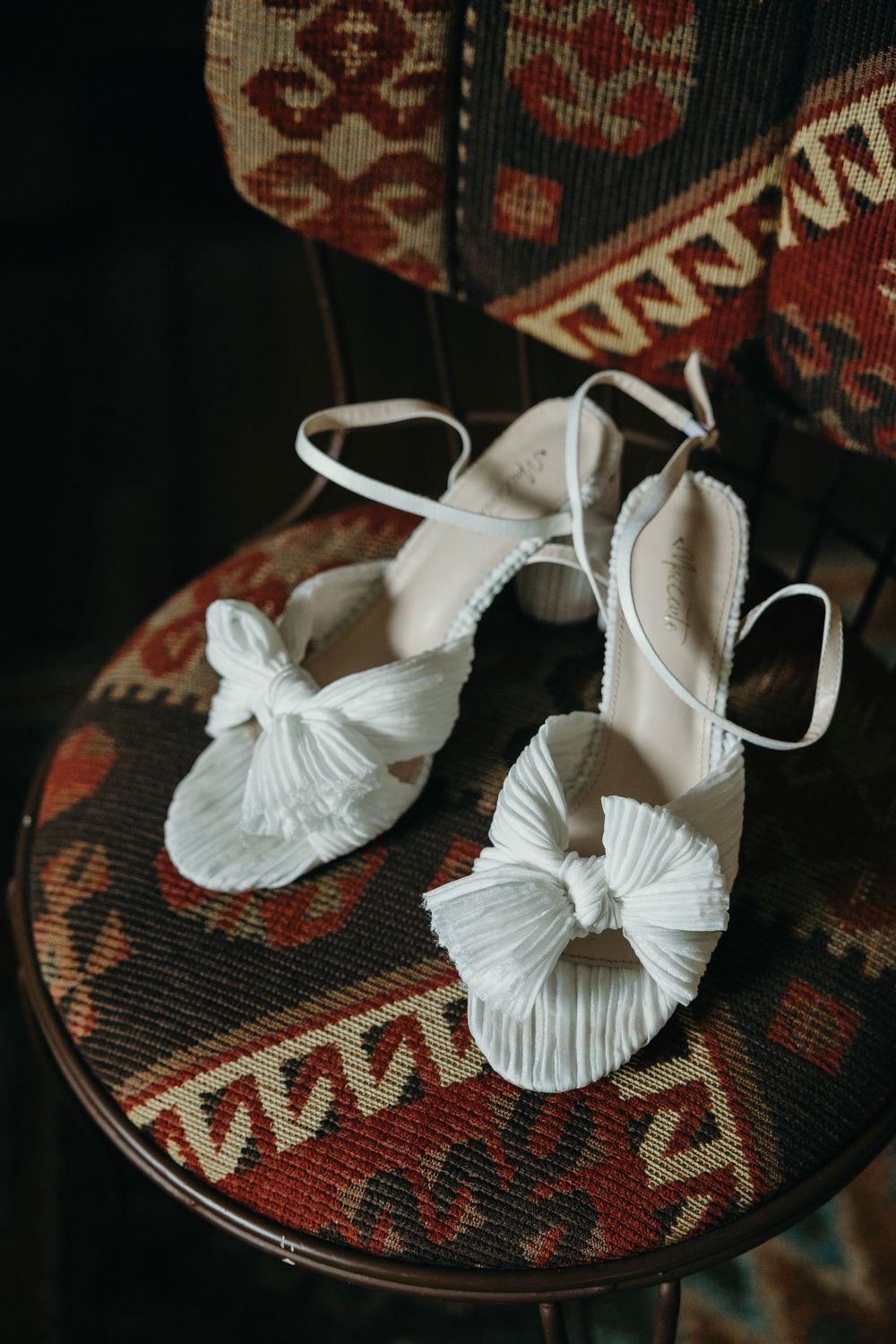 White bridal shoes with bow details displayed on patterned fabric.