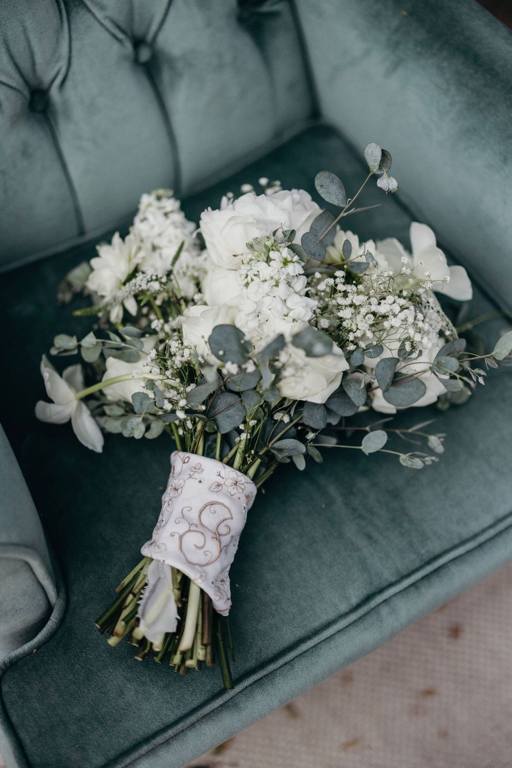 An elegant white and green wedding bouquet with eucalyptus leaves rests on a blue-grey surface.
