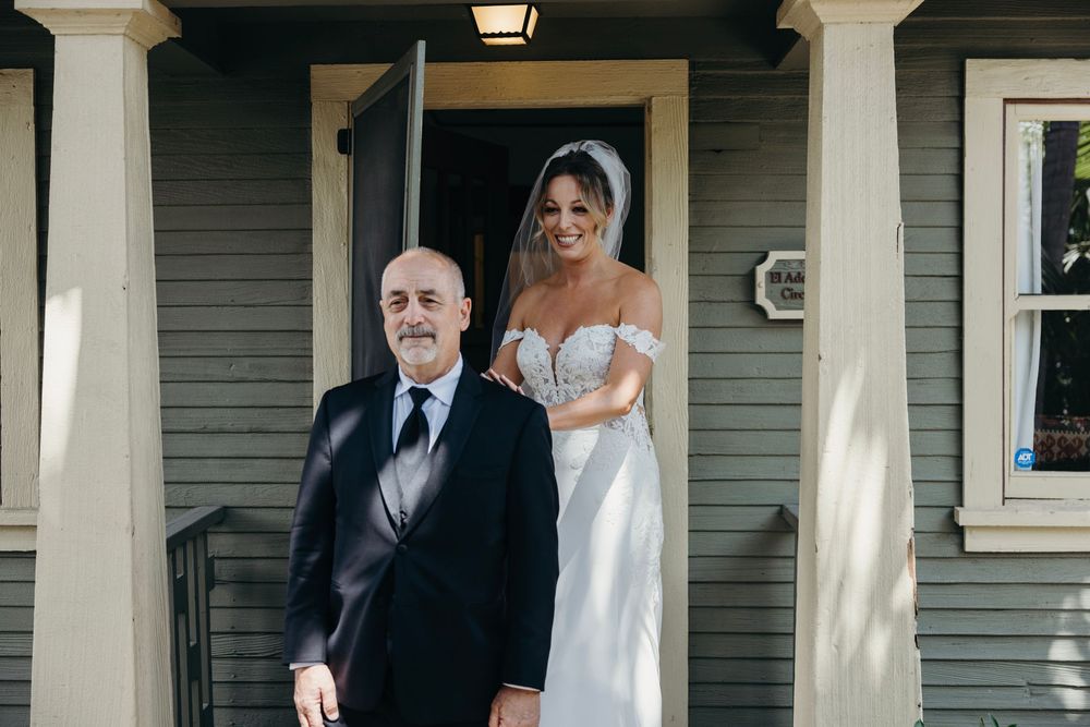 A wedding party poses on the front porch of a grey craftsman-style home.