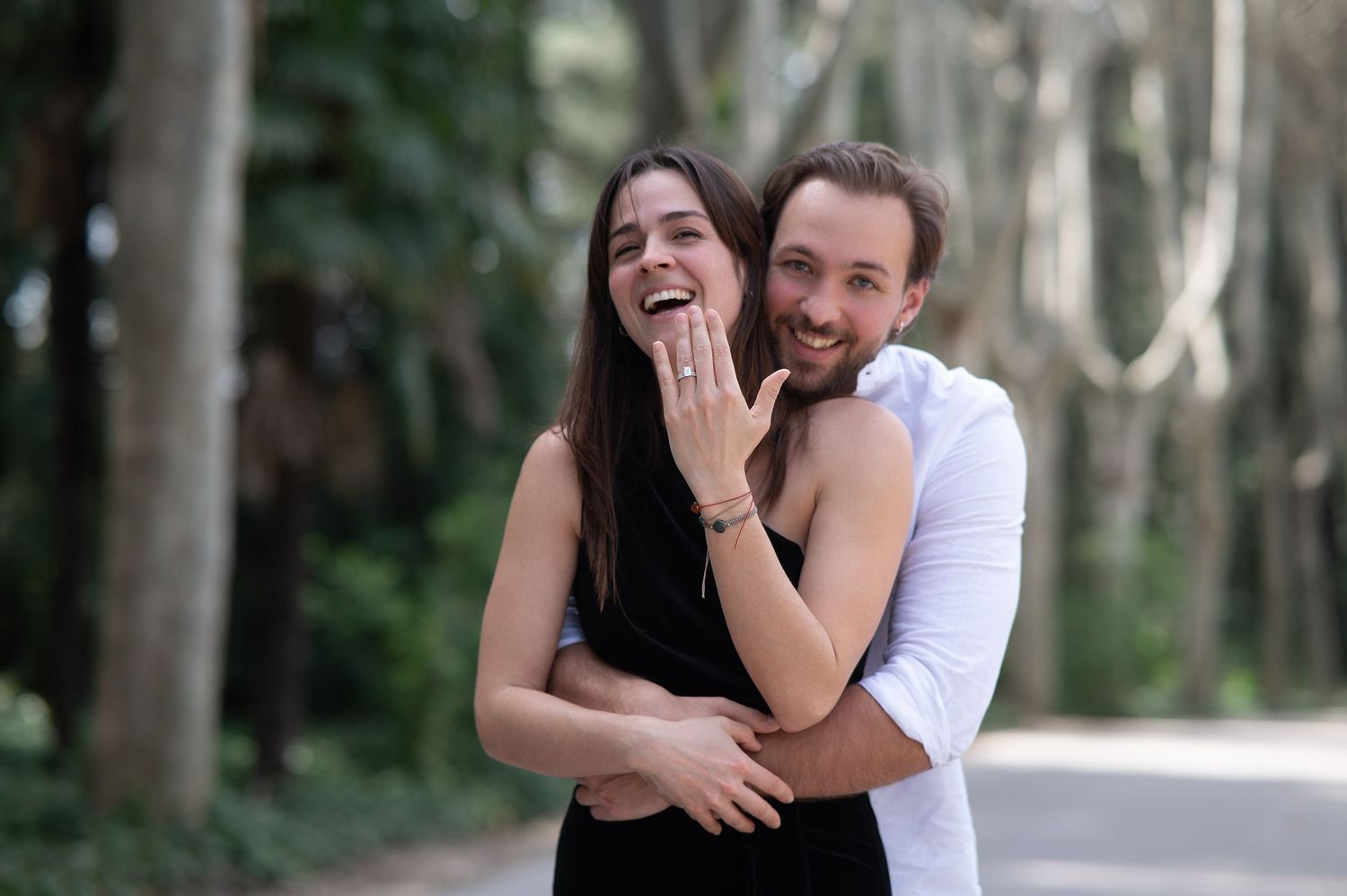 Happy couple embraces and laughs together during outdoor photo session in a wooded area.