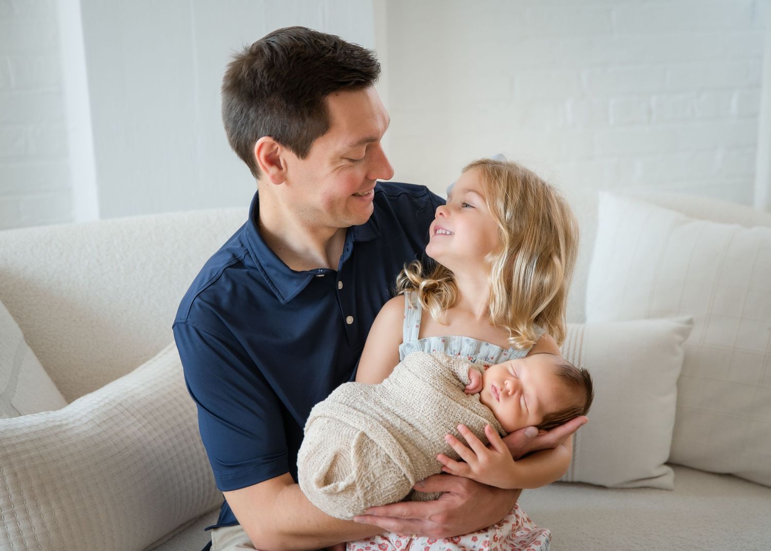 A couple shares tender moments with their baby on a white couch in a series of connected photos.
