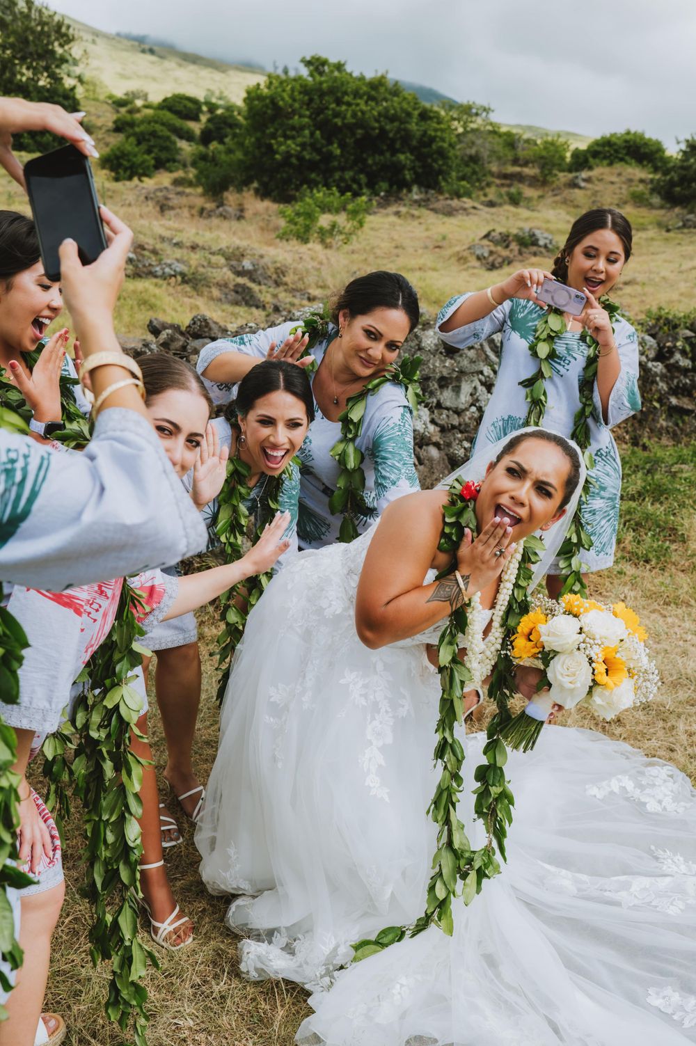 Bridesmaids in light blue dresses celebrating with bride wearing traditional white gown and floral leis.