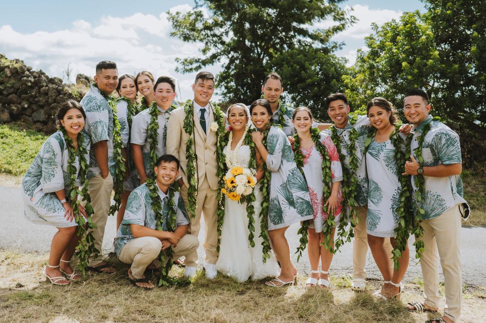 Large wedding party in coordinated attire poses along scenic mountain road.