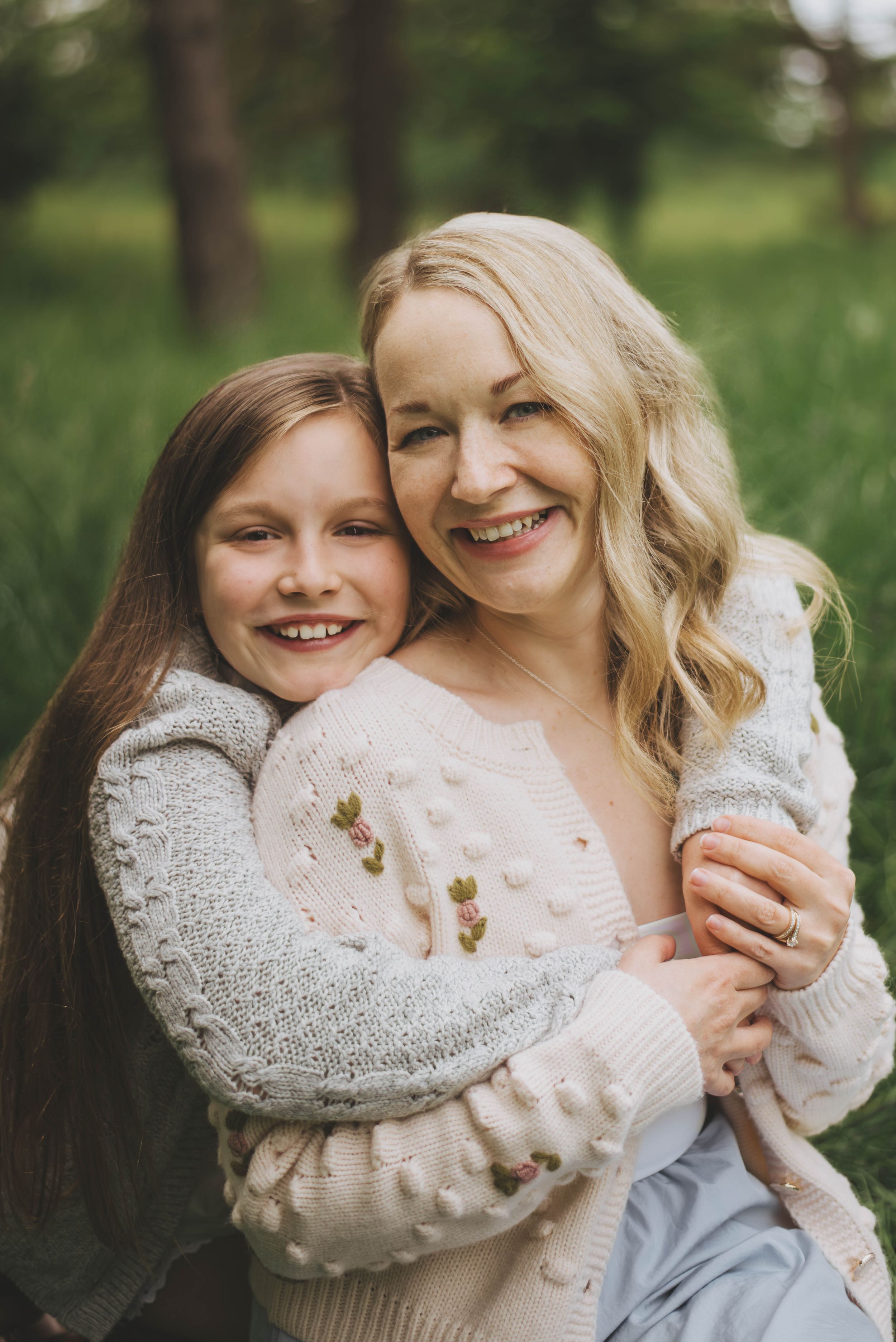 A tender moment captured in nature showing a parent embracing a smiling child in a white sweater.