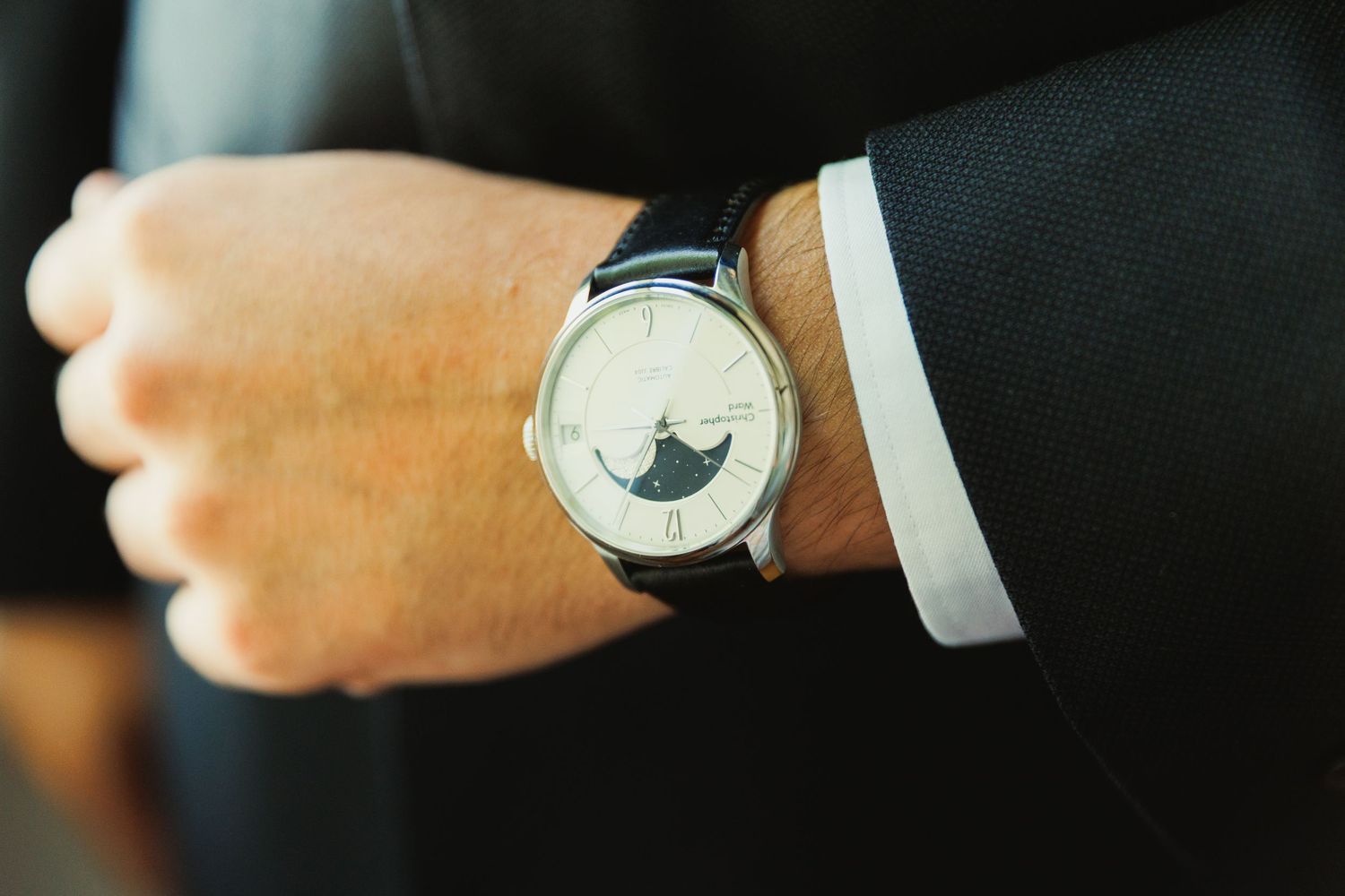 An elegant wristwatch with moon phase complication shown on a suited wrist.