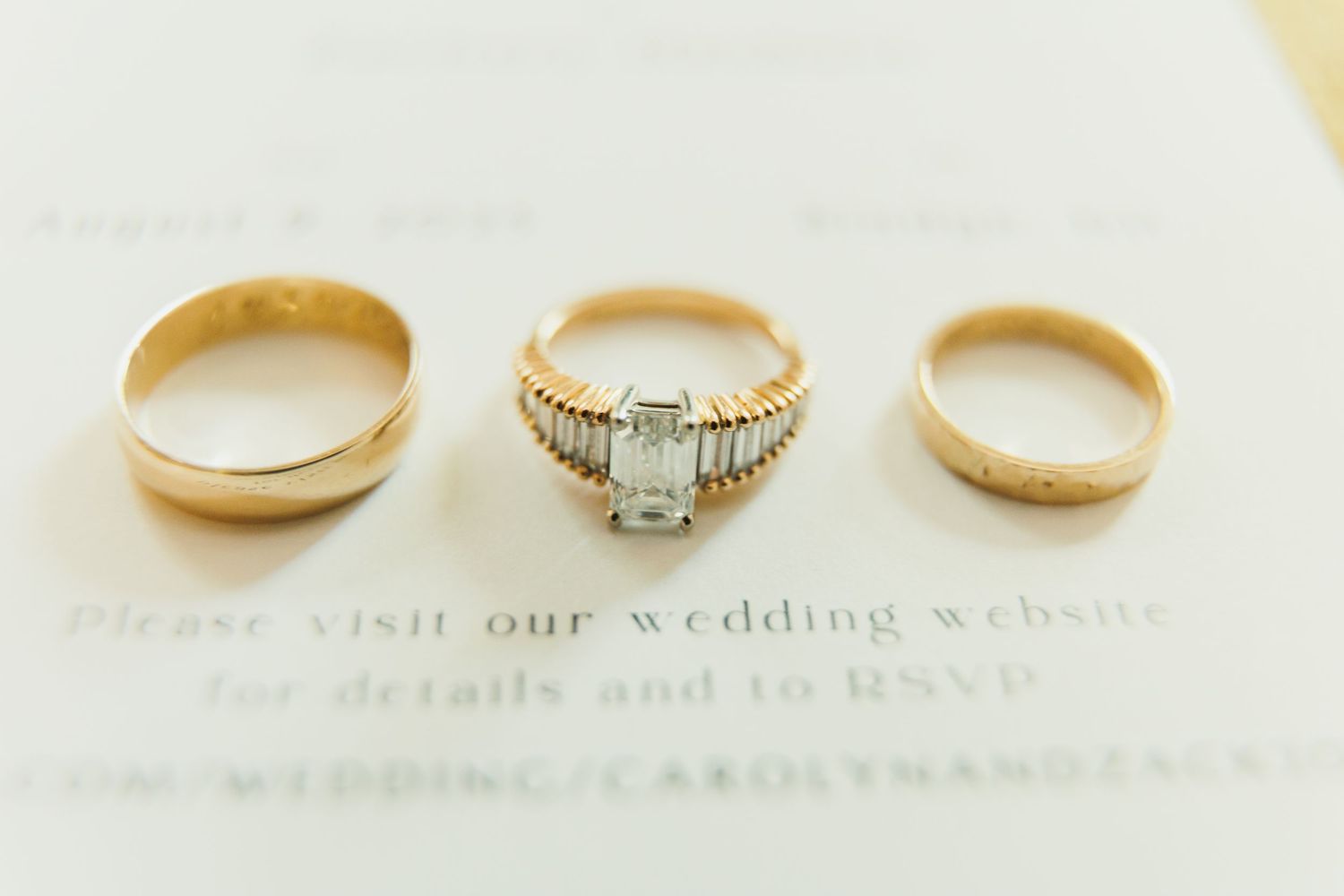 Three wedding rings including a diamond engagement ring photographed on white paper.