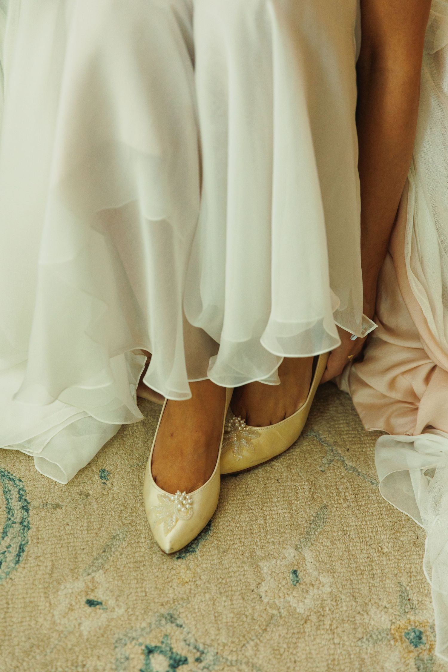 Ivory wedding shoes peek out from under layers of flowing white dress fabric.