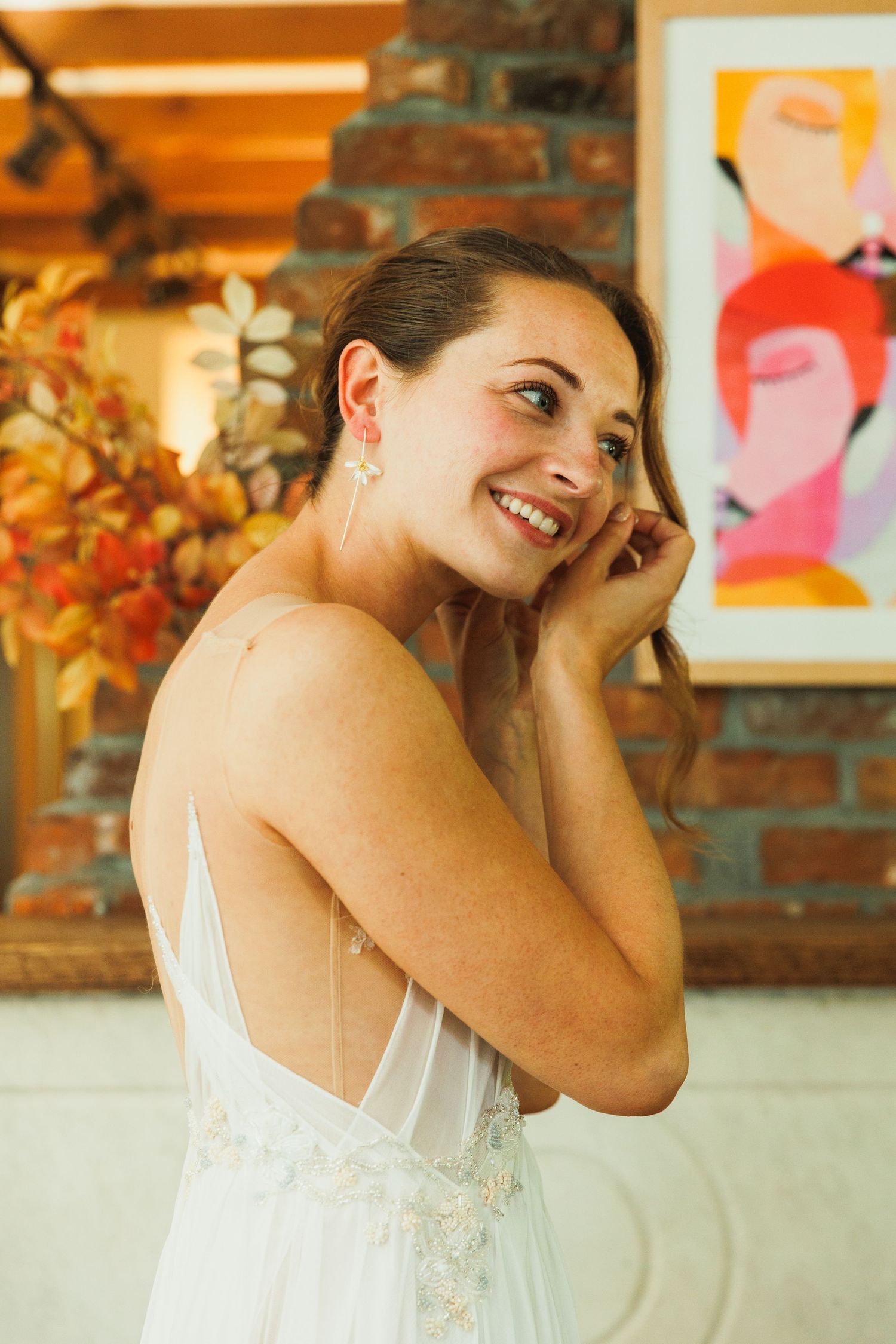 A candid moment showing someone in a white dress smiling and laughing against a brick wall with artwork.