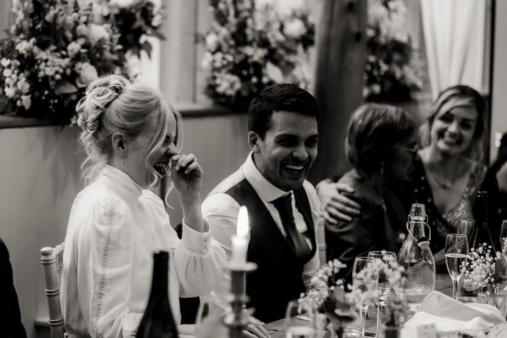 Wedding reception scene with guests laughing and celebrating around a decorated dining table.