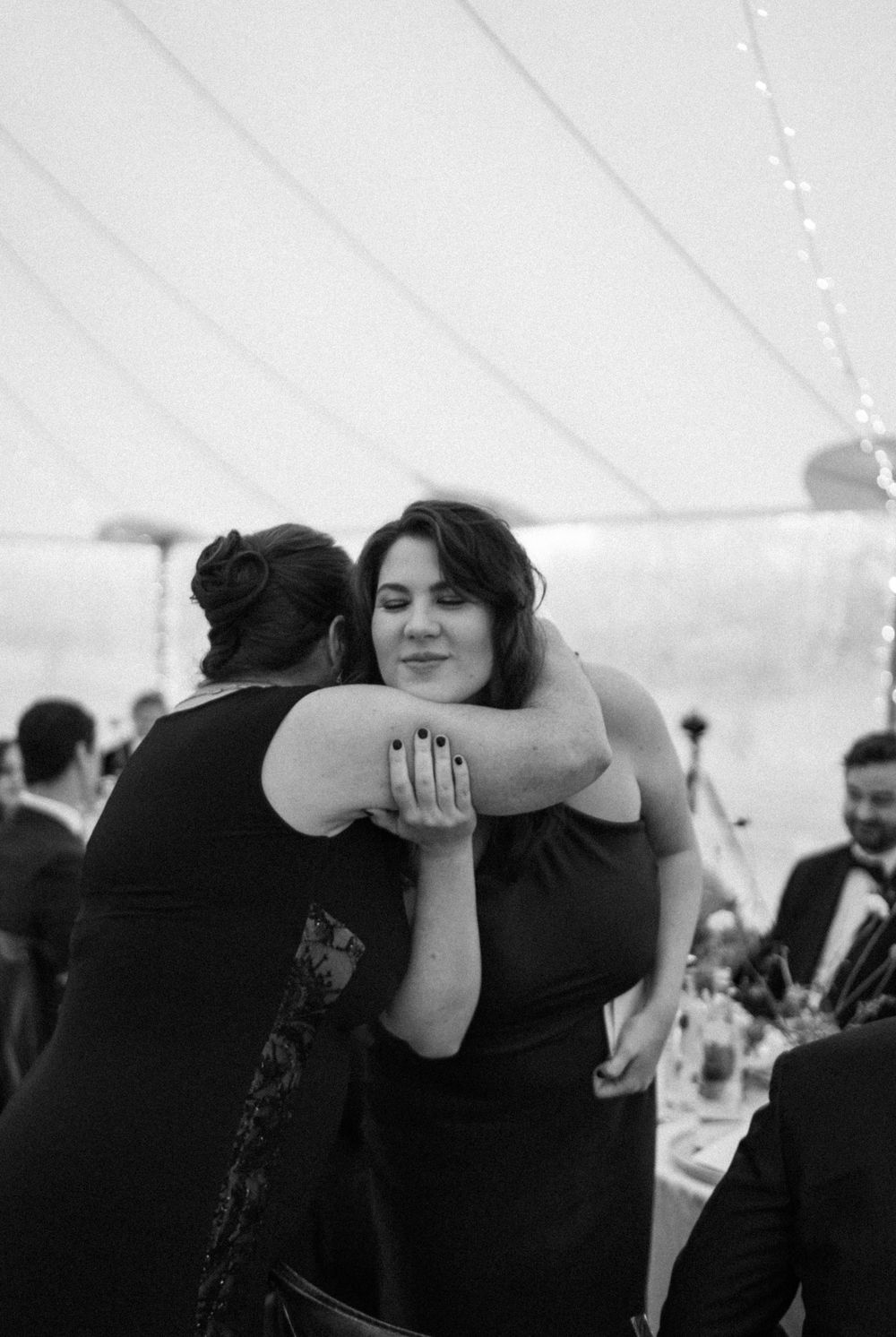 Candid hug between 2 women in a tent reception