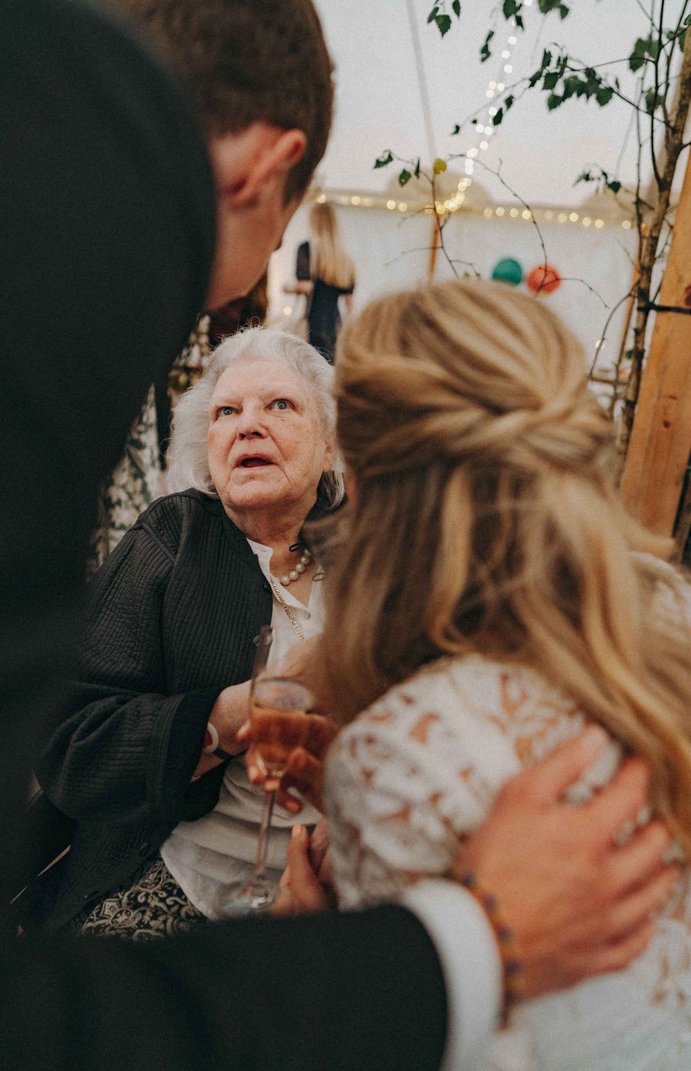 Bride & groom interacting with a grandmother seated in a wheel chair inside a tent reception