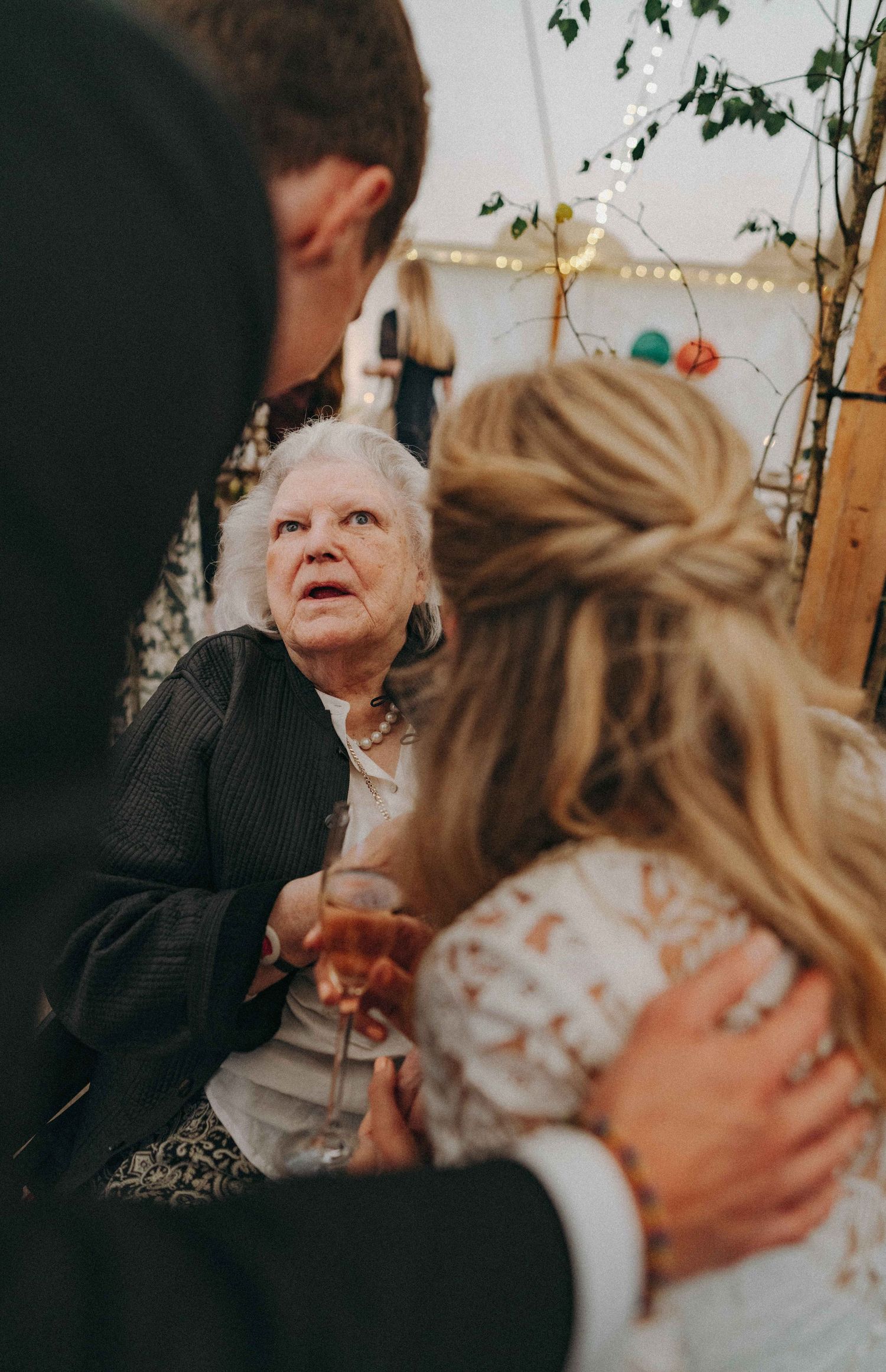 Bride & groom interacting with a grandmother seated in a wheel chair inside a tent reception