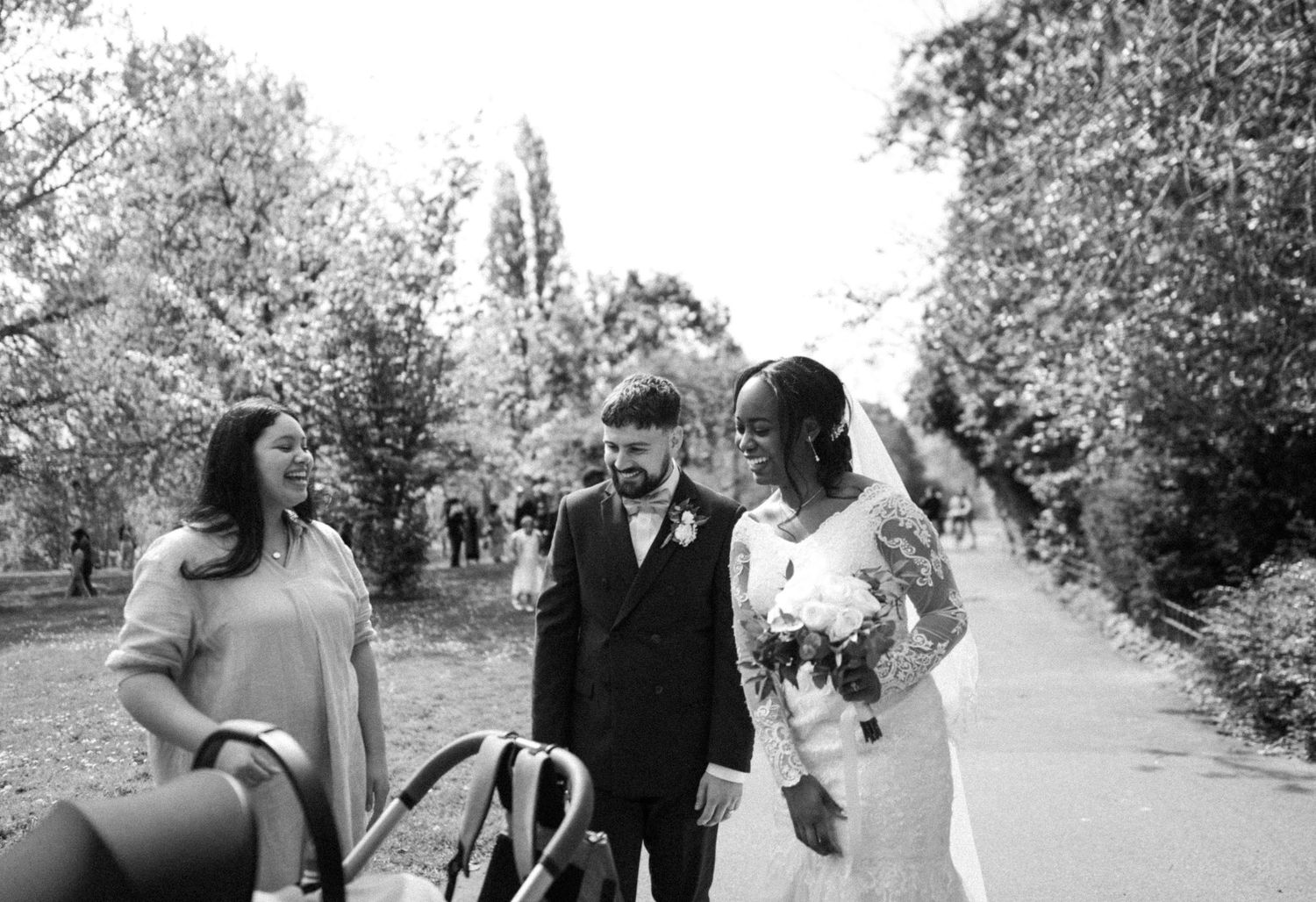 Bride and groom smiling and talking with a guest beside a stroller during a wedding