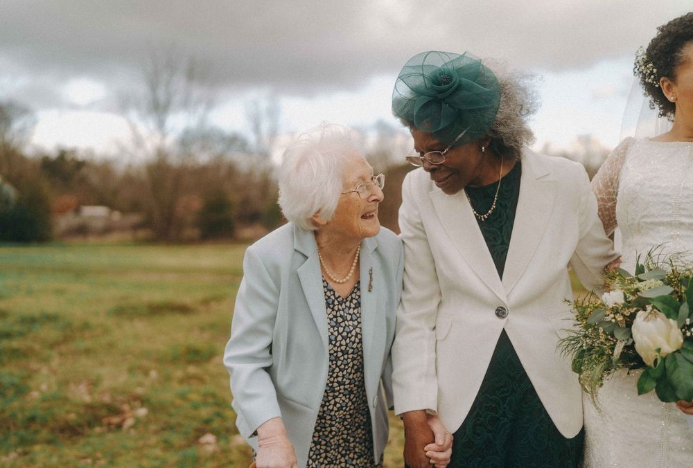 Two elderly guests holding hands and smiling with the bride during a wedding