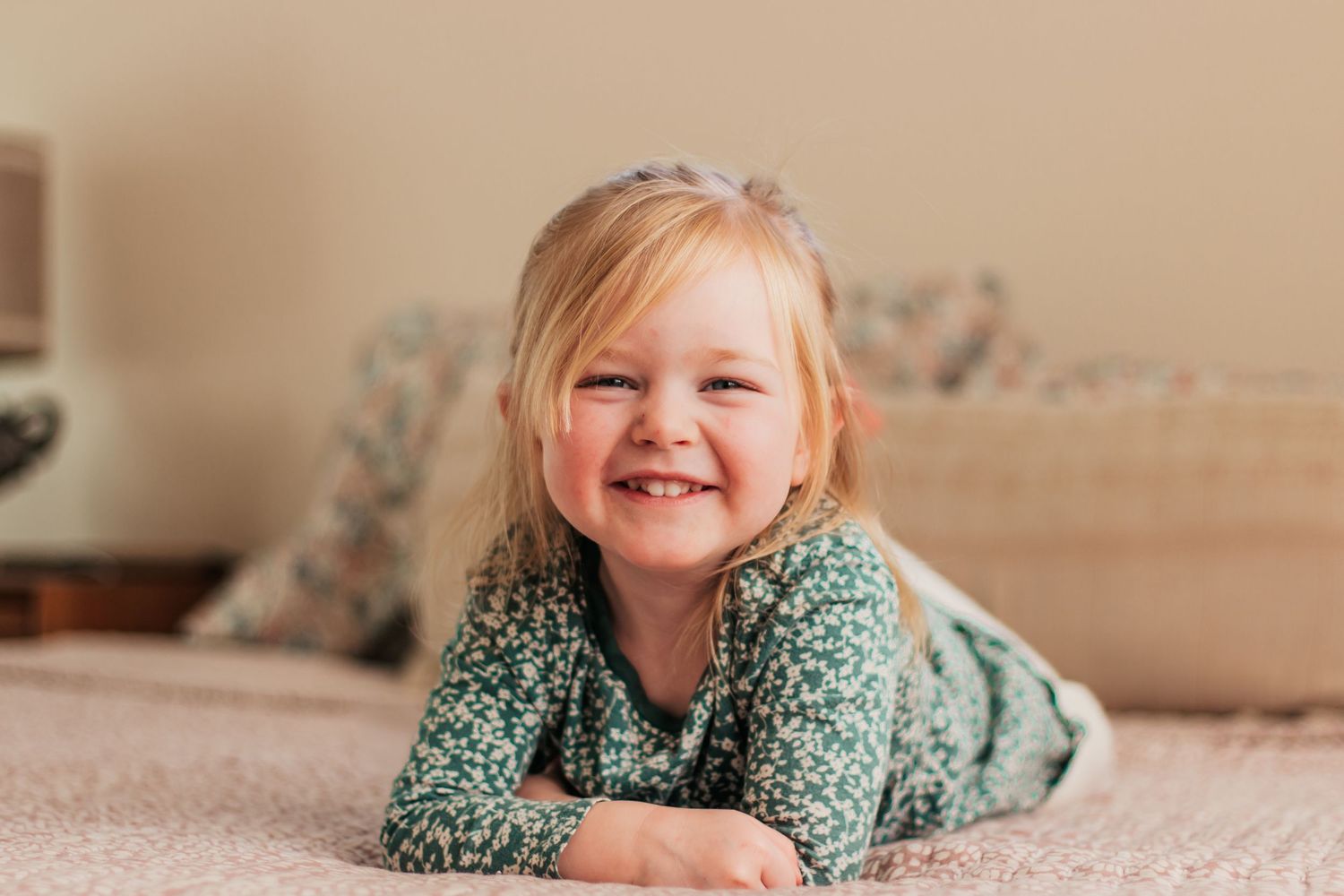 Bare feet peeking out from olive green pants while resting on a beige bedspread | Kids Birthday Photo Sessions