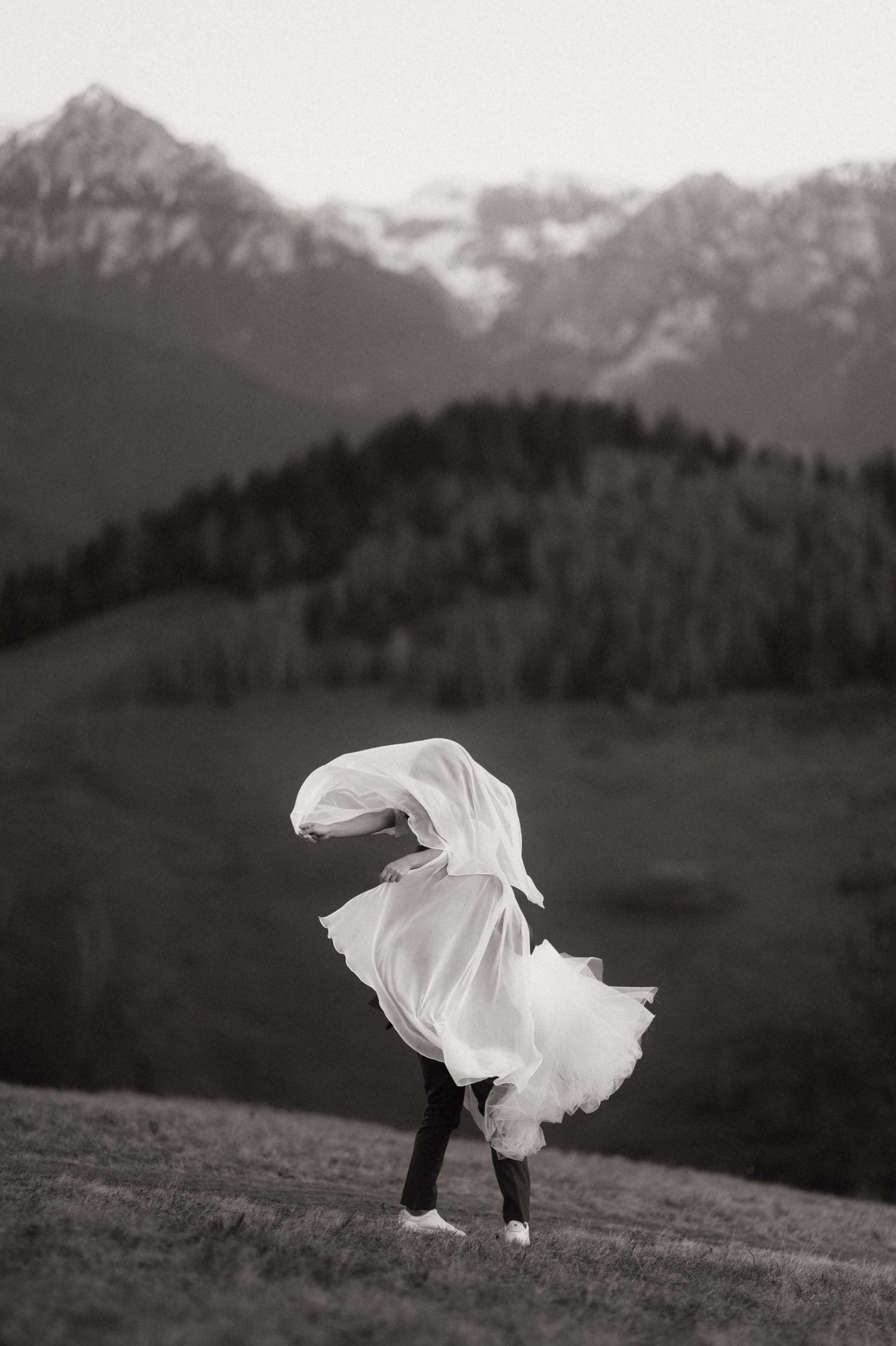 A series of black and white photographs showing a figure wrapped in white fabric moving across a hillside landscape.