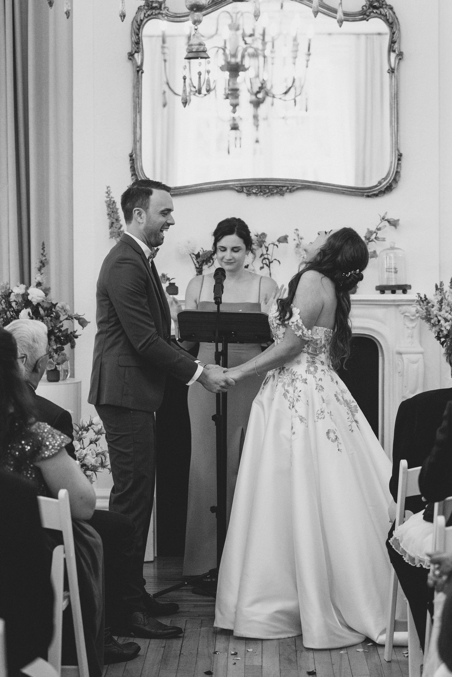 A couple shares a romantic first look moment in an elegant room with ornate mirrors and chandeliers.