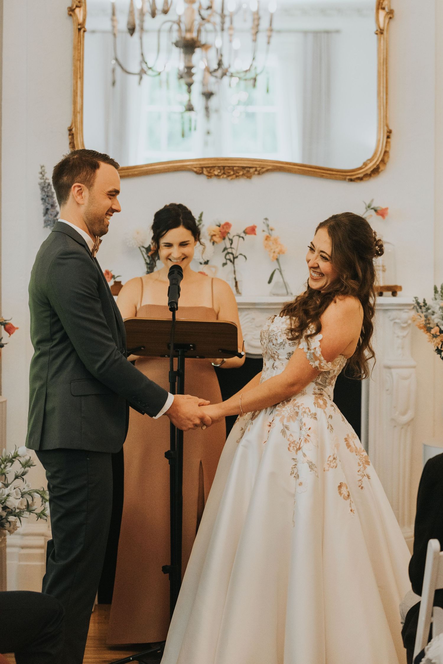 A couple laughs and embraces during their wedding first look in an elegant white ballroom.