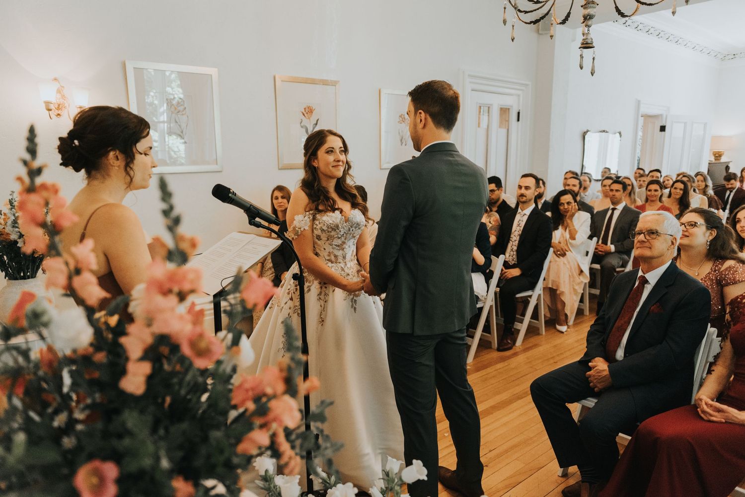 Wedding ceremony guests seated in rows watch the proceedings in an elegant ballroom with floral decor.