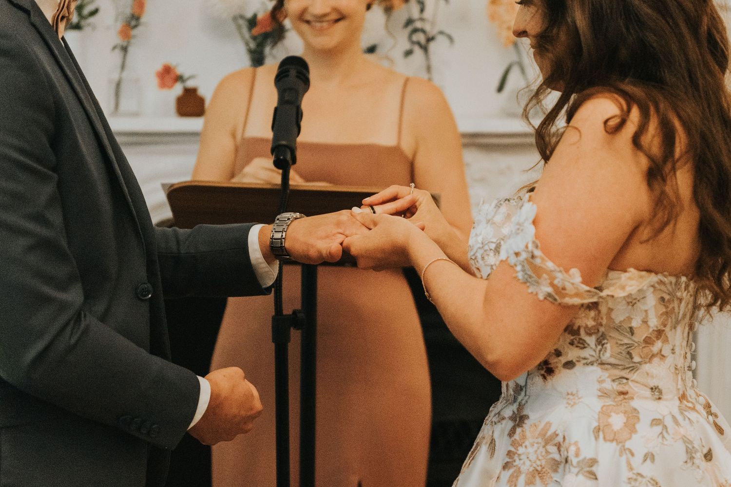 A wedding ceremony moment showing hands exchanging rings in an elegant indoor setting.