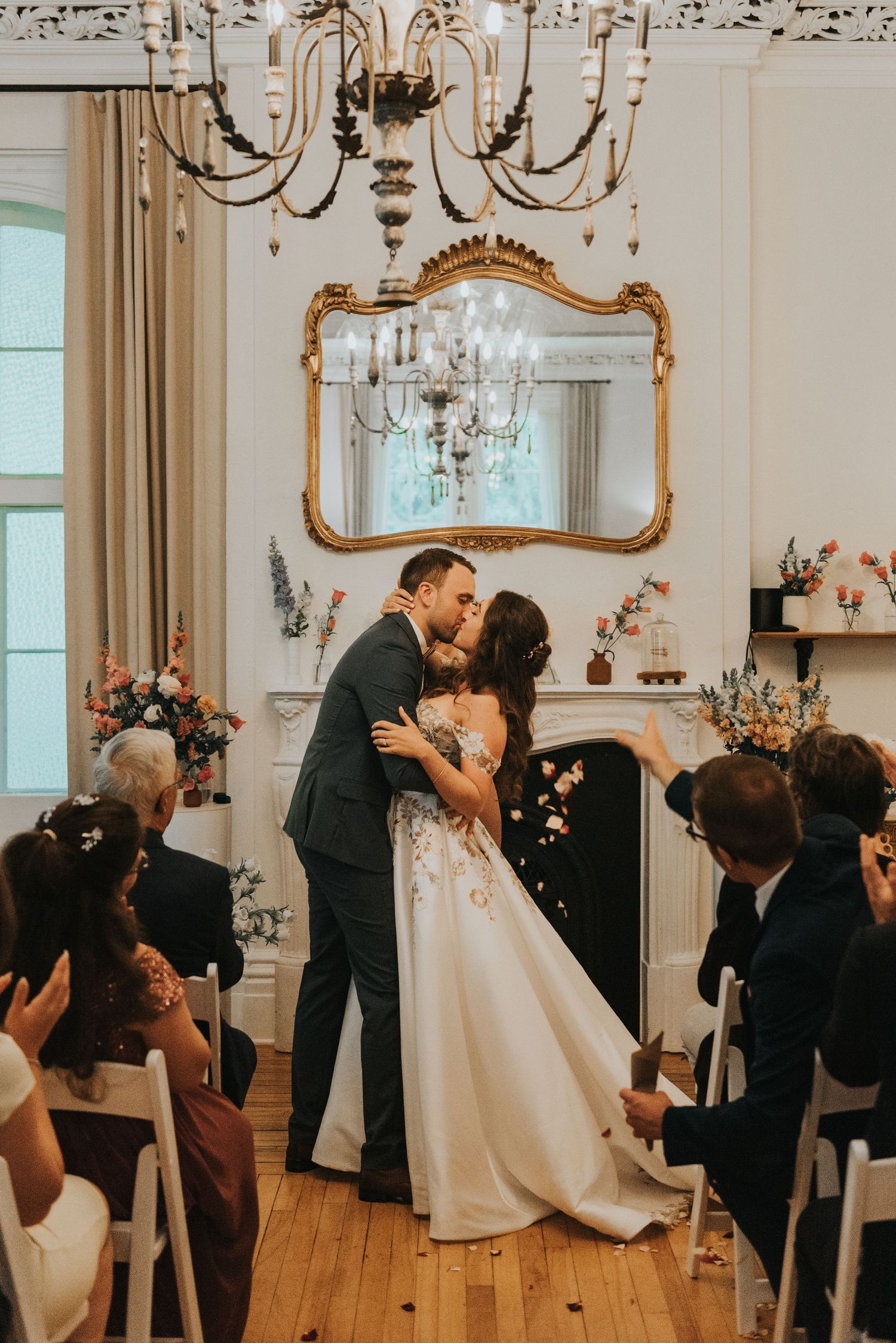A romantic wedding ceremony kiss captured in a sequence of four elegant photos in a white room with chandeliers.