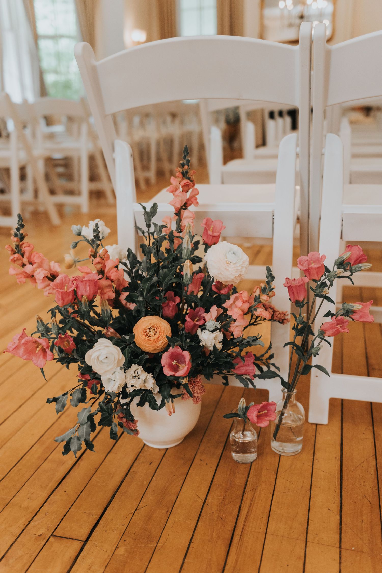 Elegant floral centerpieces with pink and white flowers arranged in white vases on wooden tables at a wedding reception.