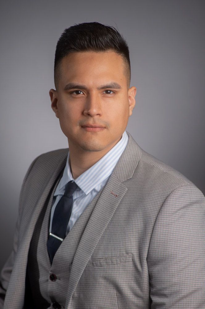 Professional man wearing a gray houndstooth blazer and striped shirt with a dark tie against a gray background.