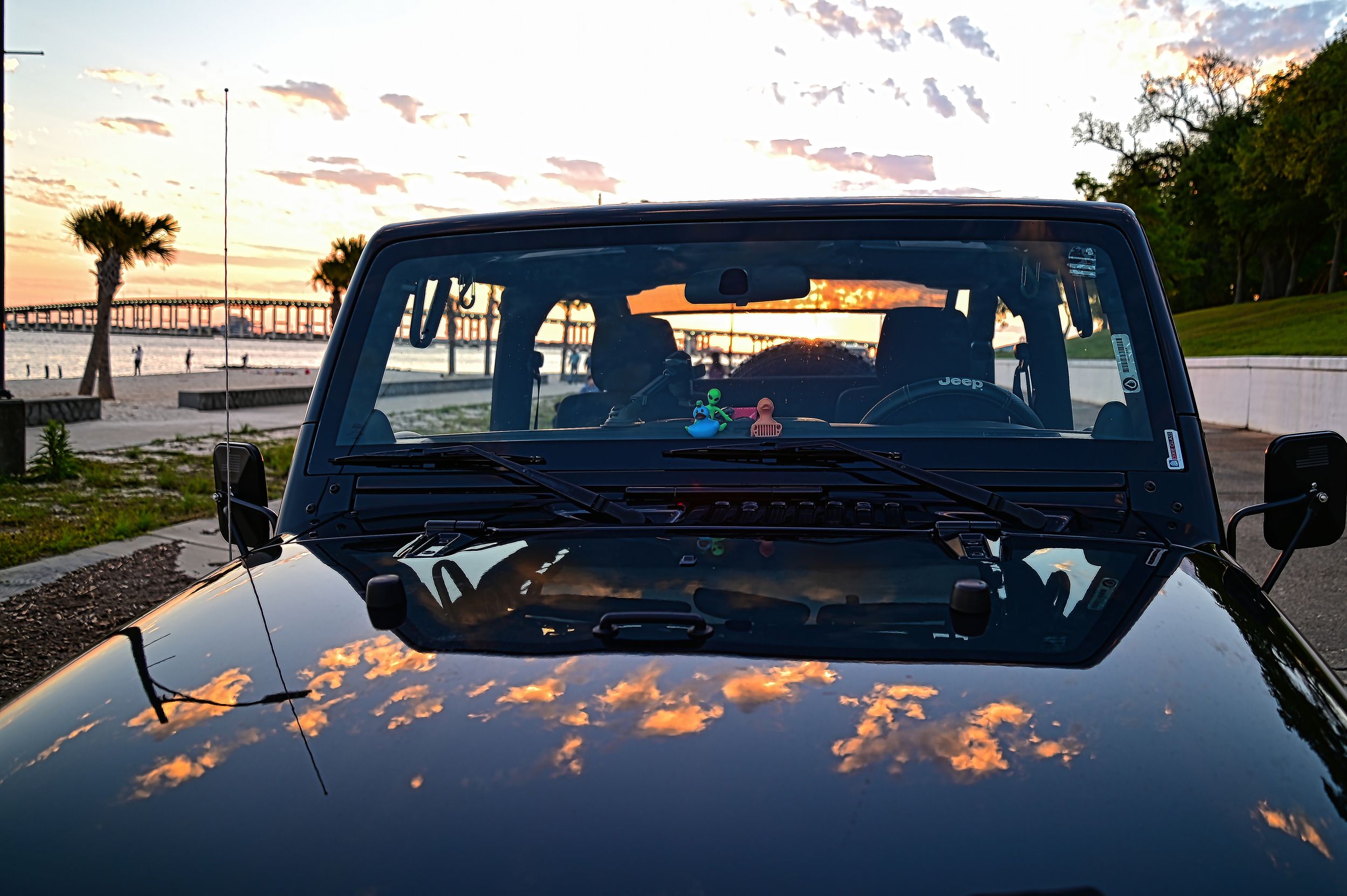 Jeep Wrangler hood reflecting sunset clouds at Ocean Springs Mississippi beach with the Biloxi Bridge in background