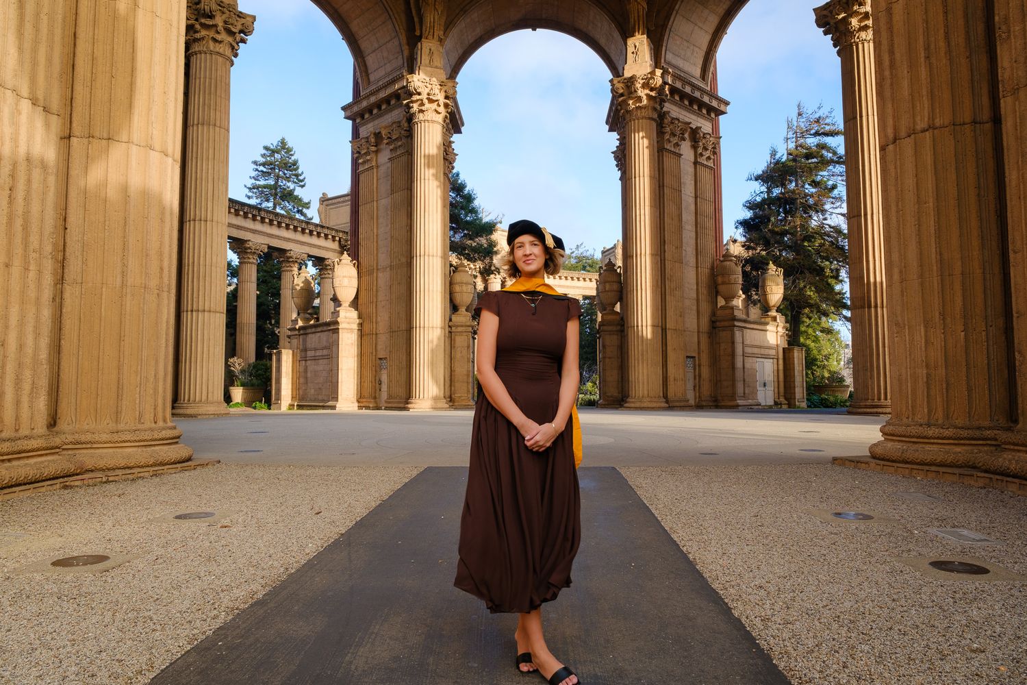 Woman in brown maxi dress poses at Palace of Fine Arts colonnade, San Francisco, golden hour light.