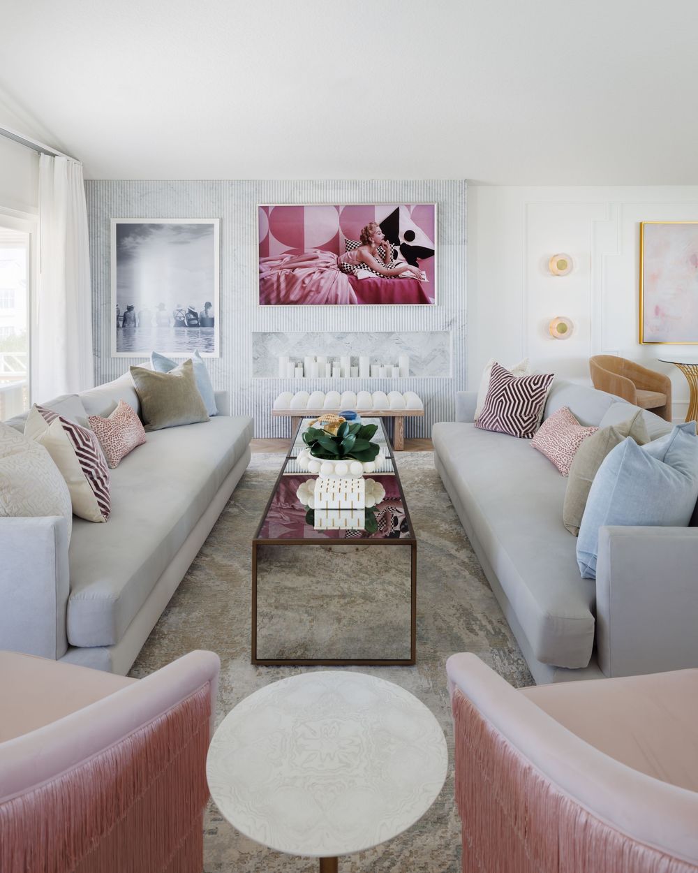 Bright living room with gray sofas, pink fringe chairs, mirrored coffee table, and bold pink pop art above fireplace.