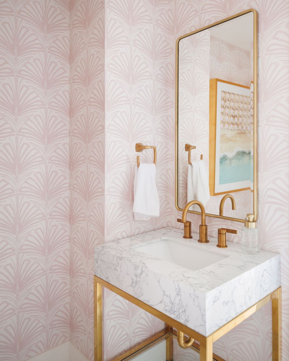 Pink Art Deco wallpaper bathroom with marble sink, gold fixtures, and a rectangular gold-framed mirror.