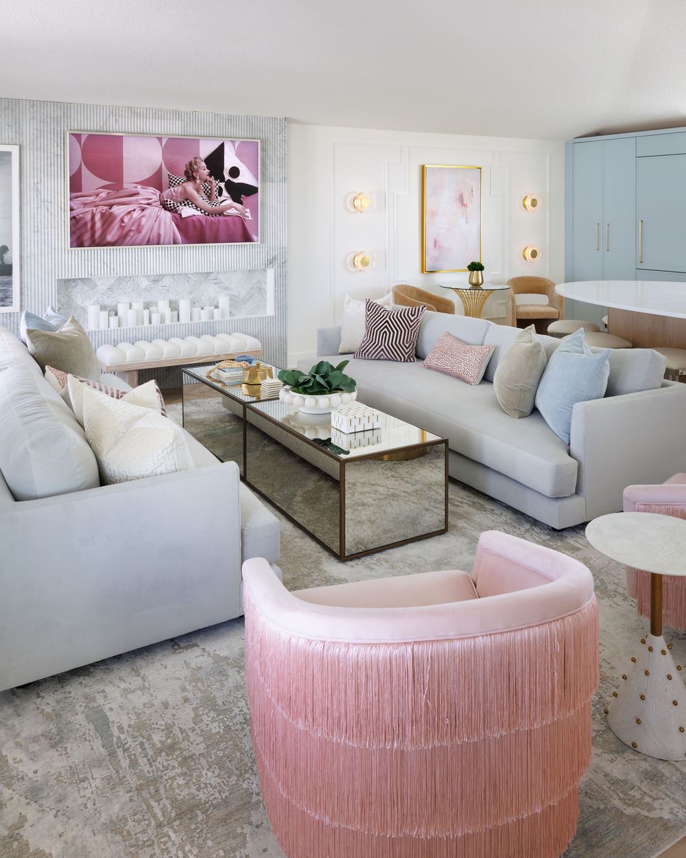Elegant living room featuring gray sofas, pink fringe accent chairs, mirrored coffee table, and vibrant pop art wall decor.