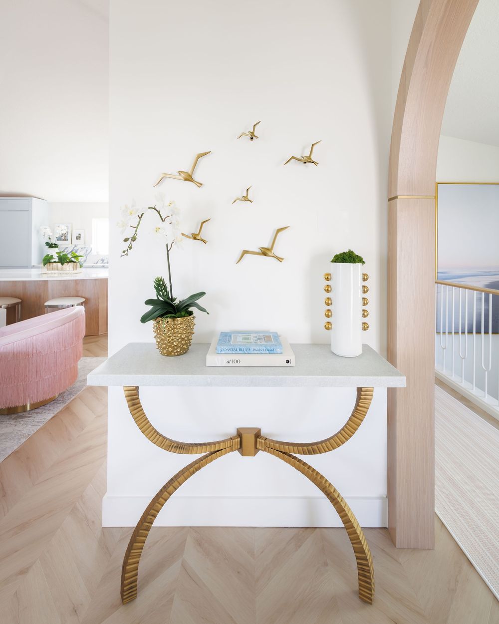 Bright coastal entryway with white gold console table, brass bird wall art, and arched wood trim.
